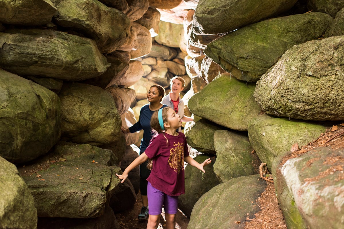 Family walking through narrow stone grotto on trail