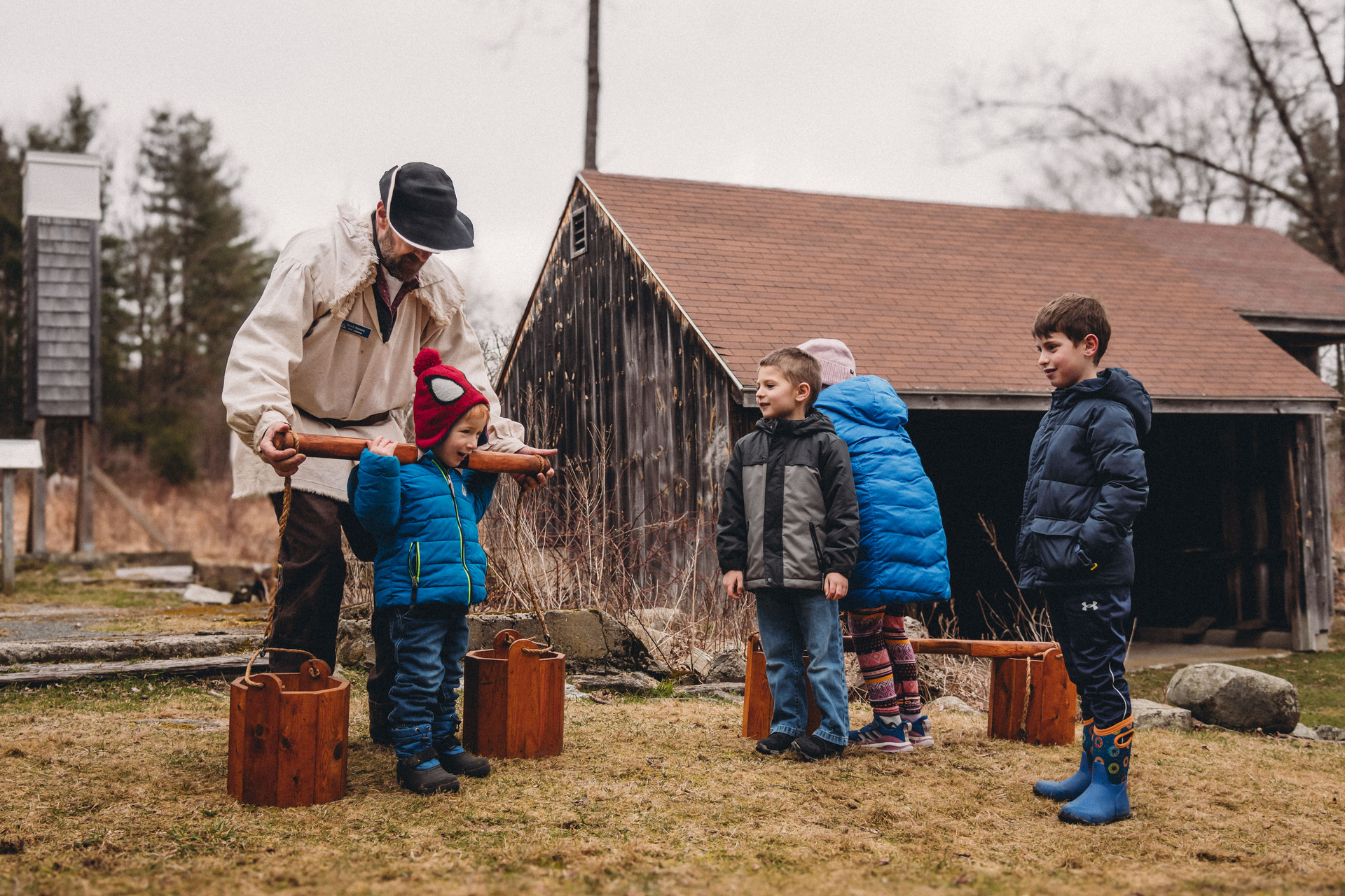 Children trying on old maple sugaring equipment