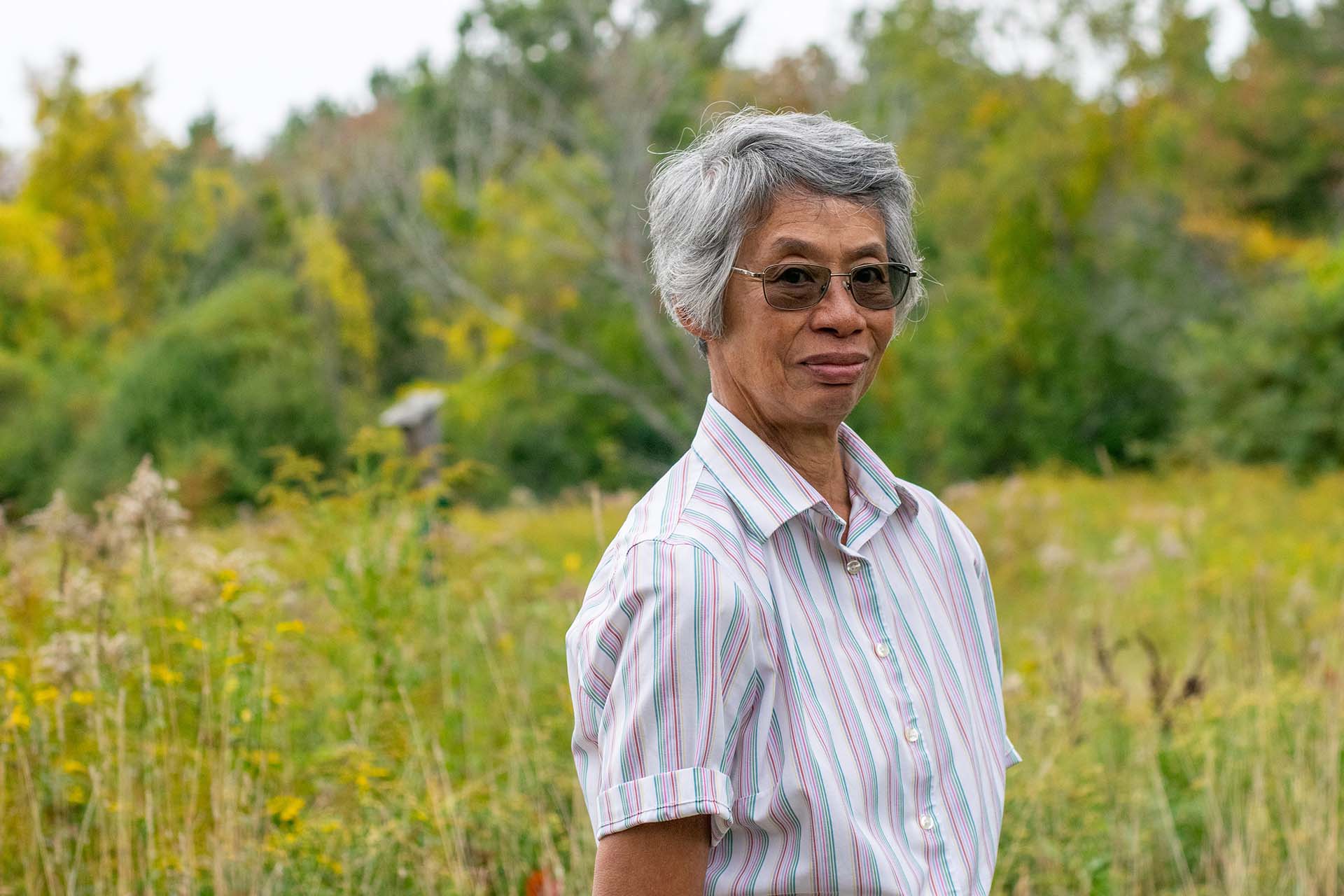 Woman with short gray hair and a button up shirt standing in a green meadow.