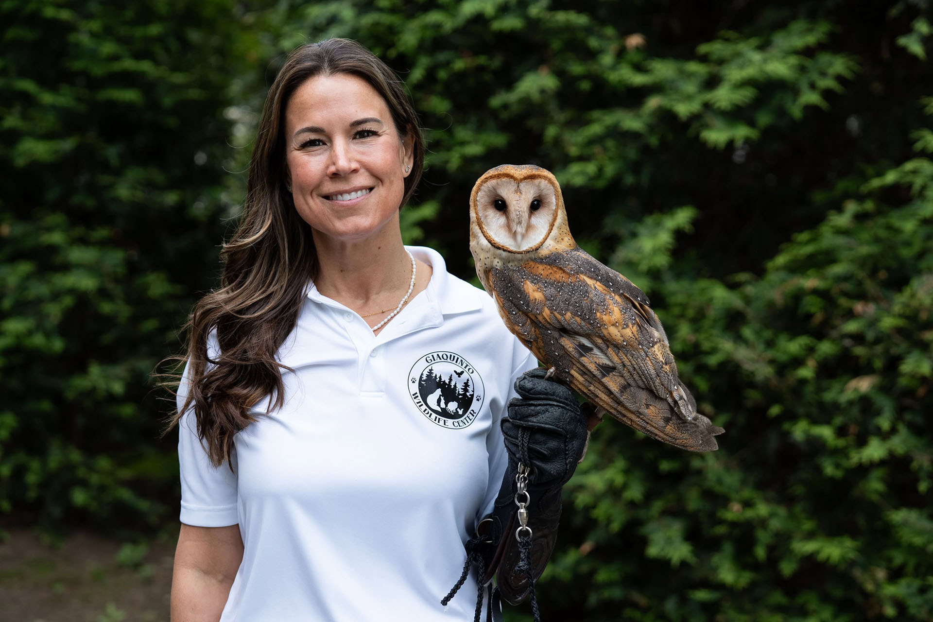 A smiling woman with a barn owl perched on a black glove
