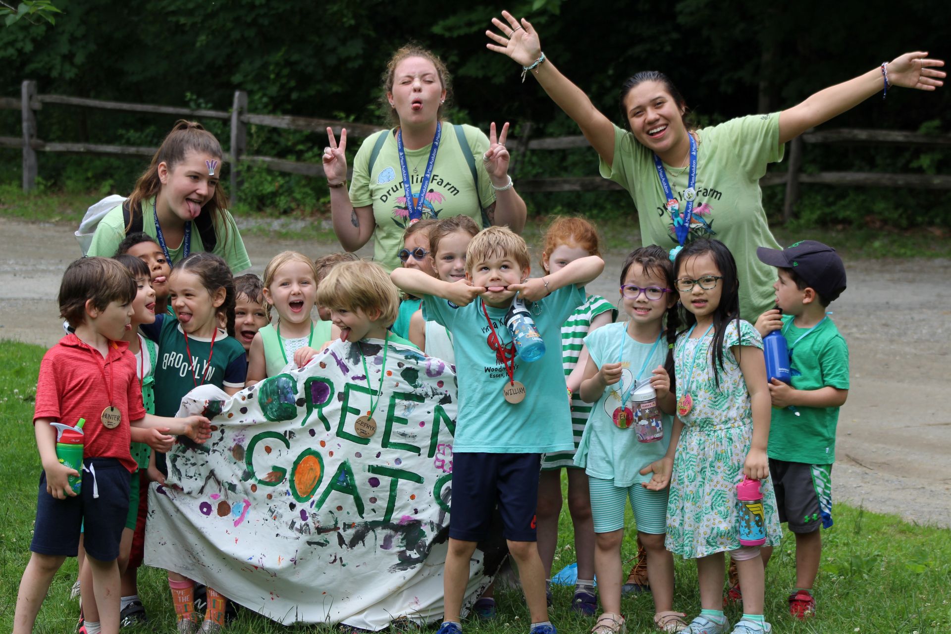 Three counselors make silly faces and smile with a group of small campers.