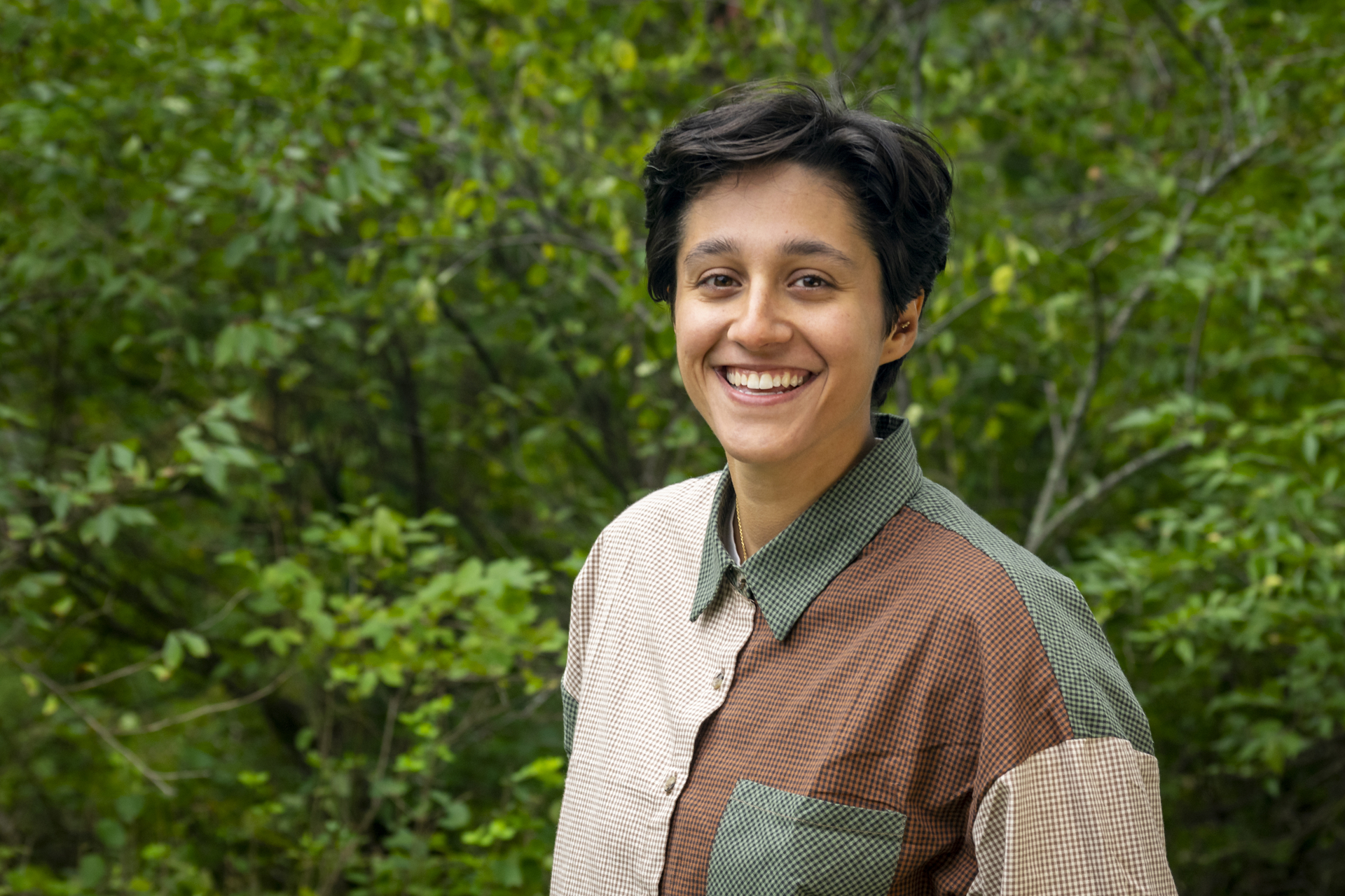 Amara wearing a color-blocked button down, smiling with trees in the background.