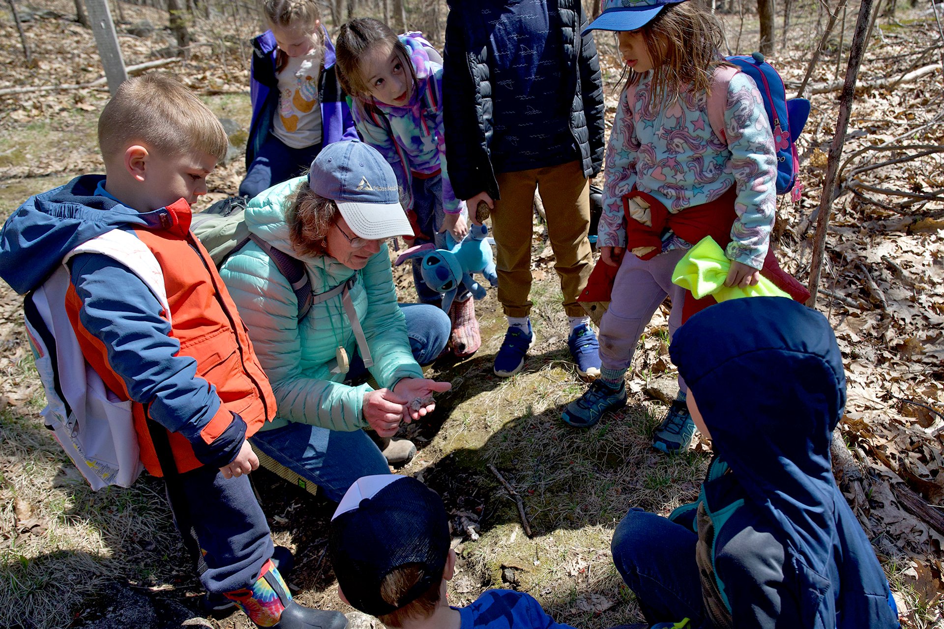 Educator showing a group of children a leaf or stick in their hand