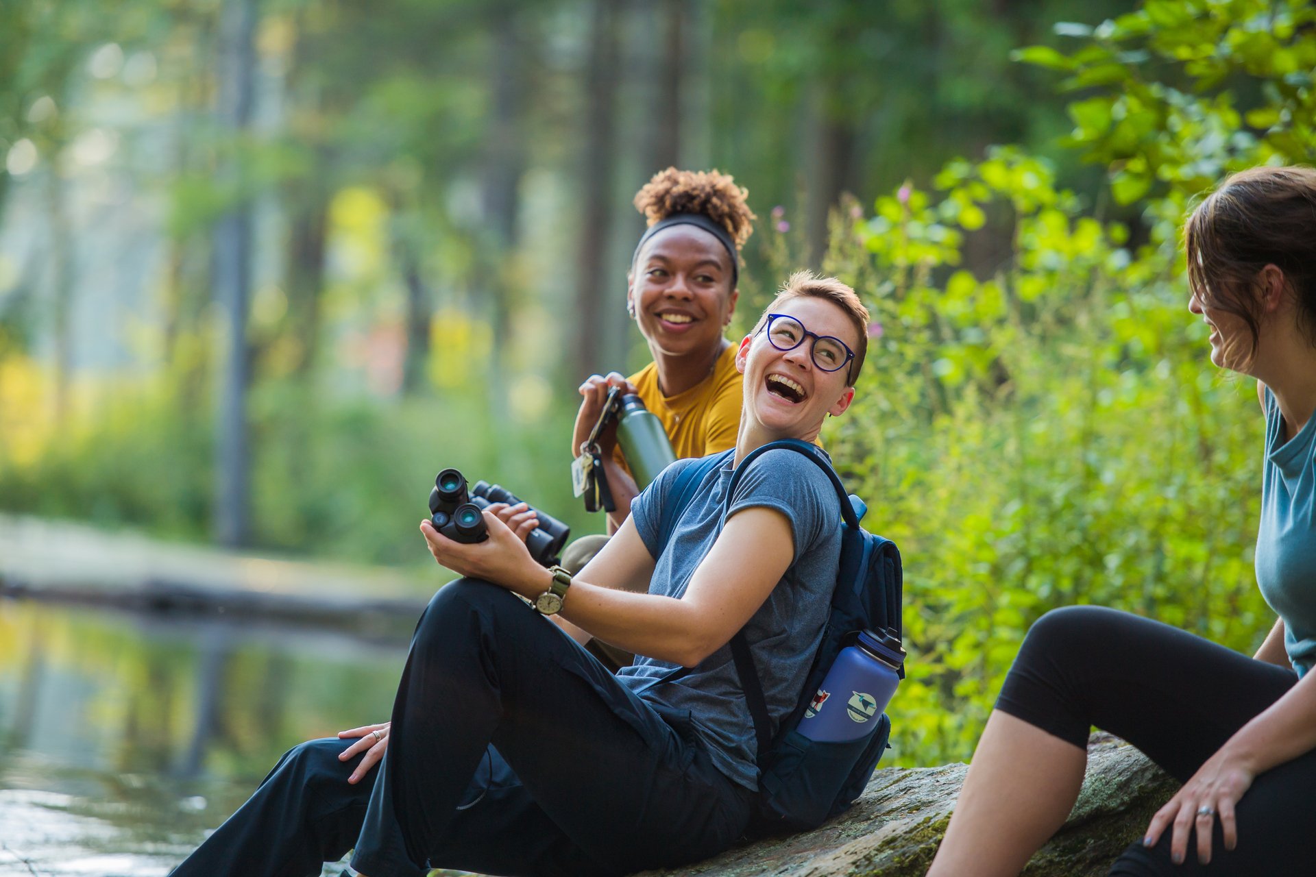 Three people sitting on a rock holding binoculars and laughing