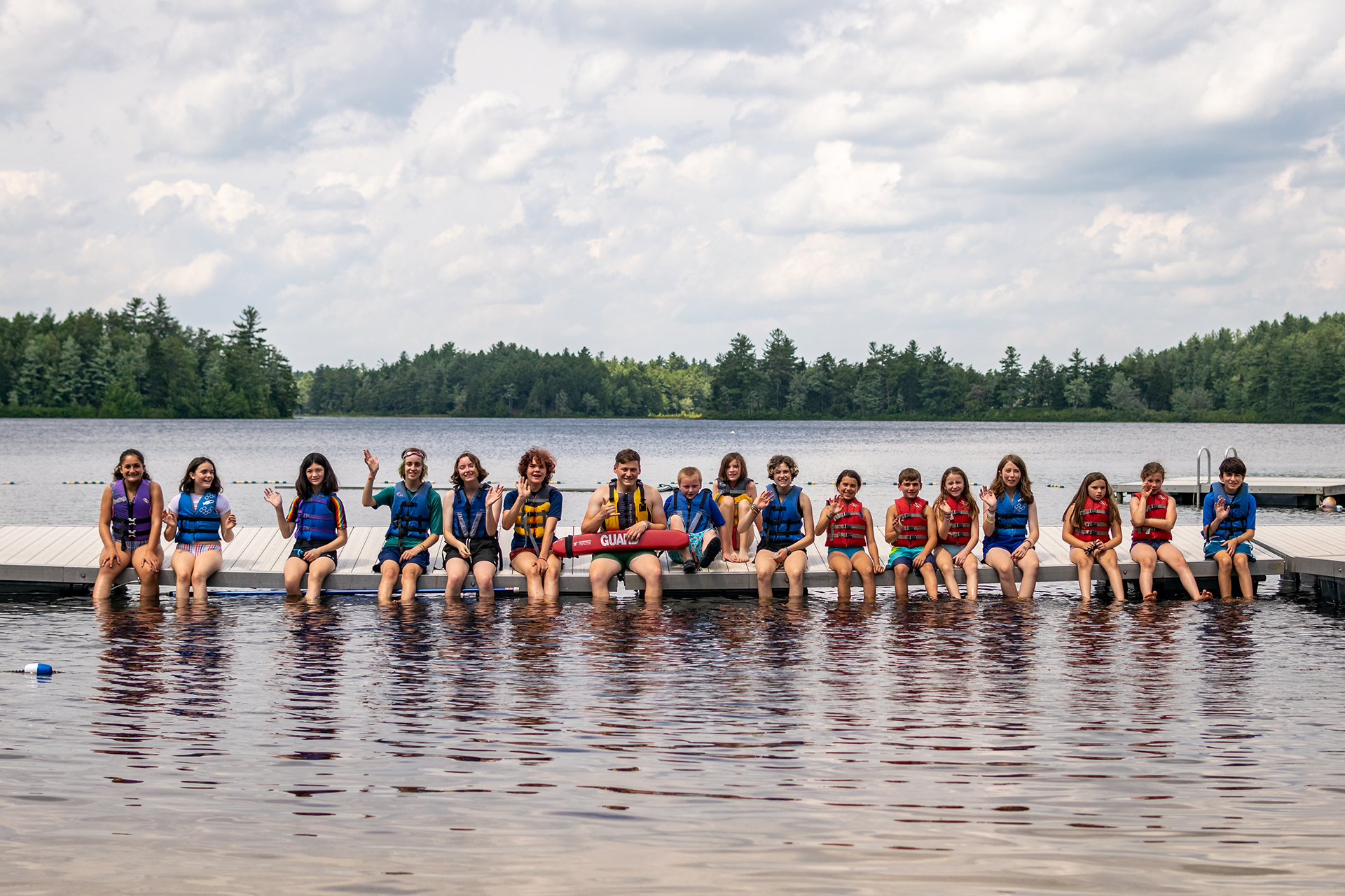 Campers and lifeguard sitting on the dock with their feet in the water