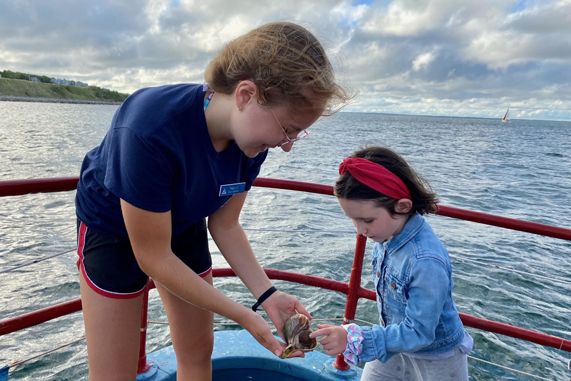 An educator showing a shell to a young child at the bow of a boat