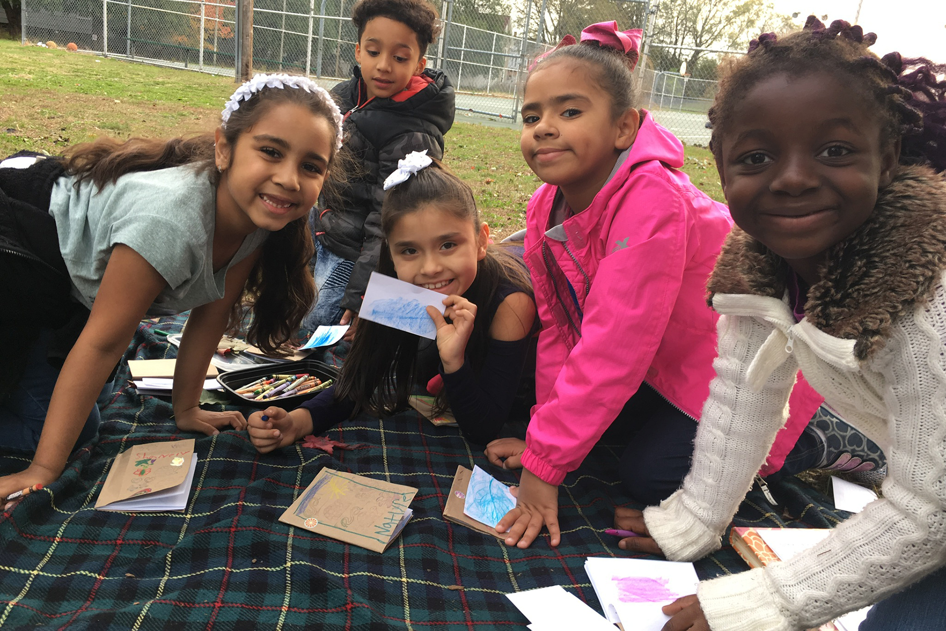 Students making leaf rubbings on a blanket outside