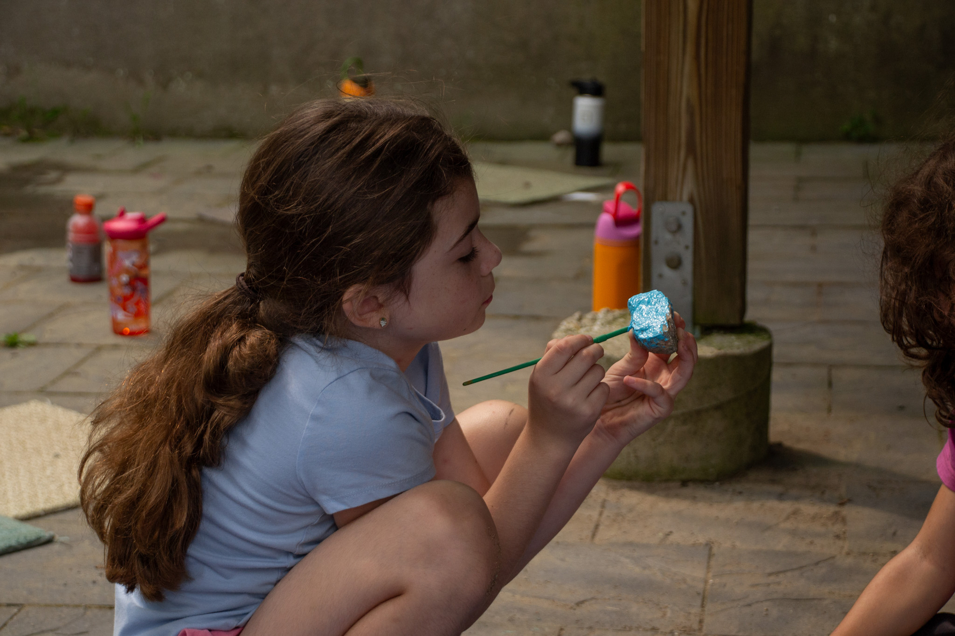 camper crouches and paints a rock blue with a paintbrush