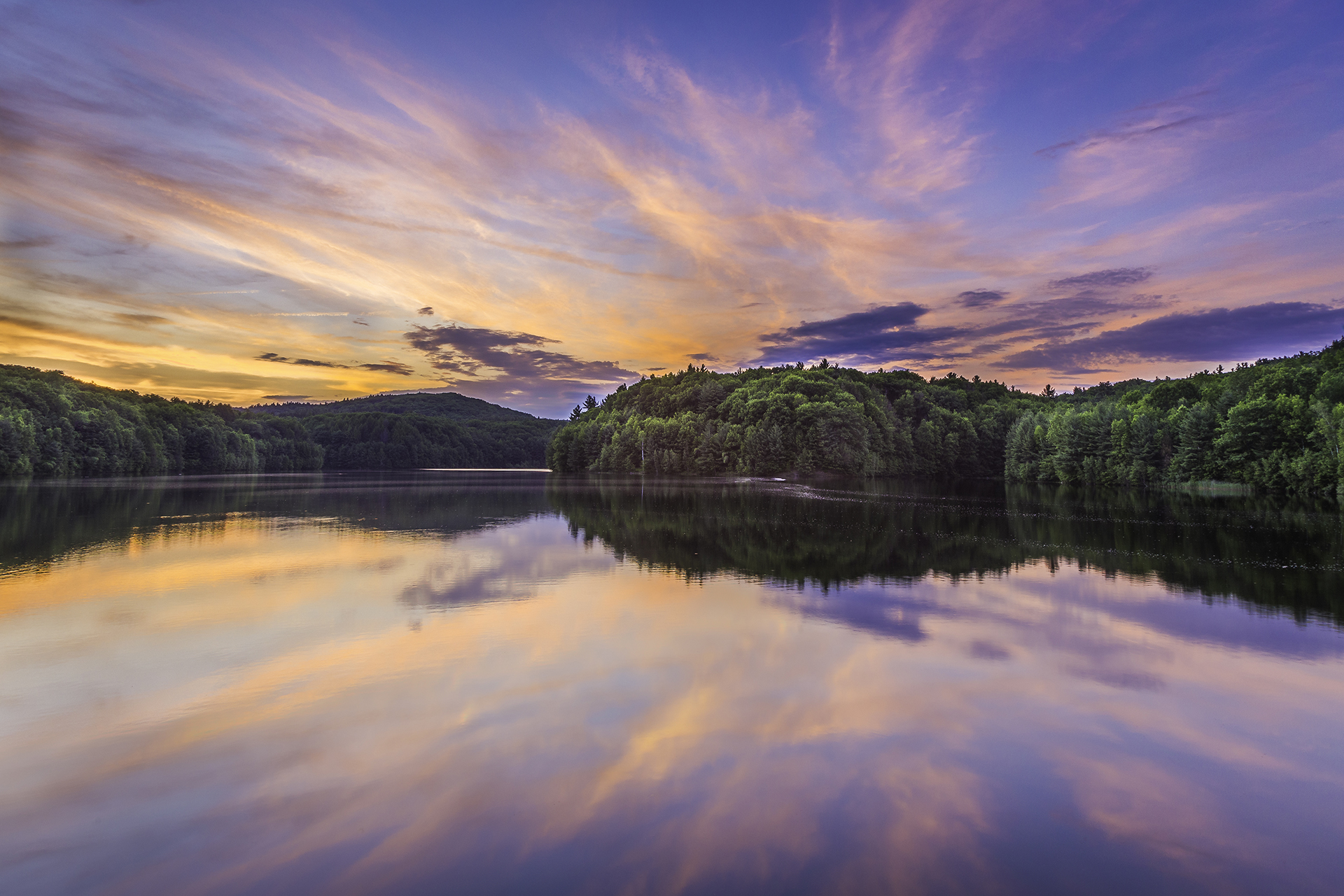 Purple and yellow sunset reflected over a lake with trees