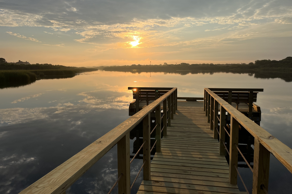 A boardwalk onto a lake, facing a sun set.