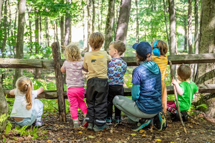 Preschoolers and a teacher leaning on a fence