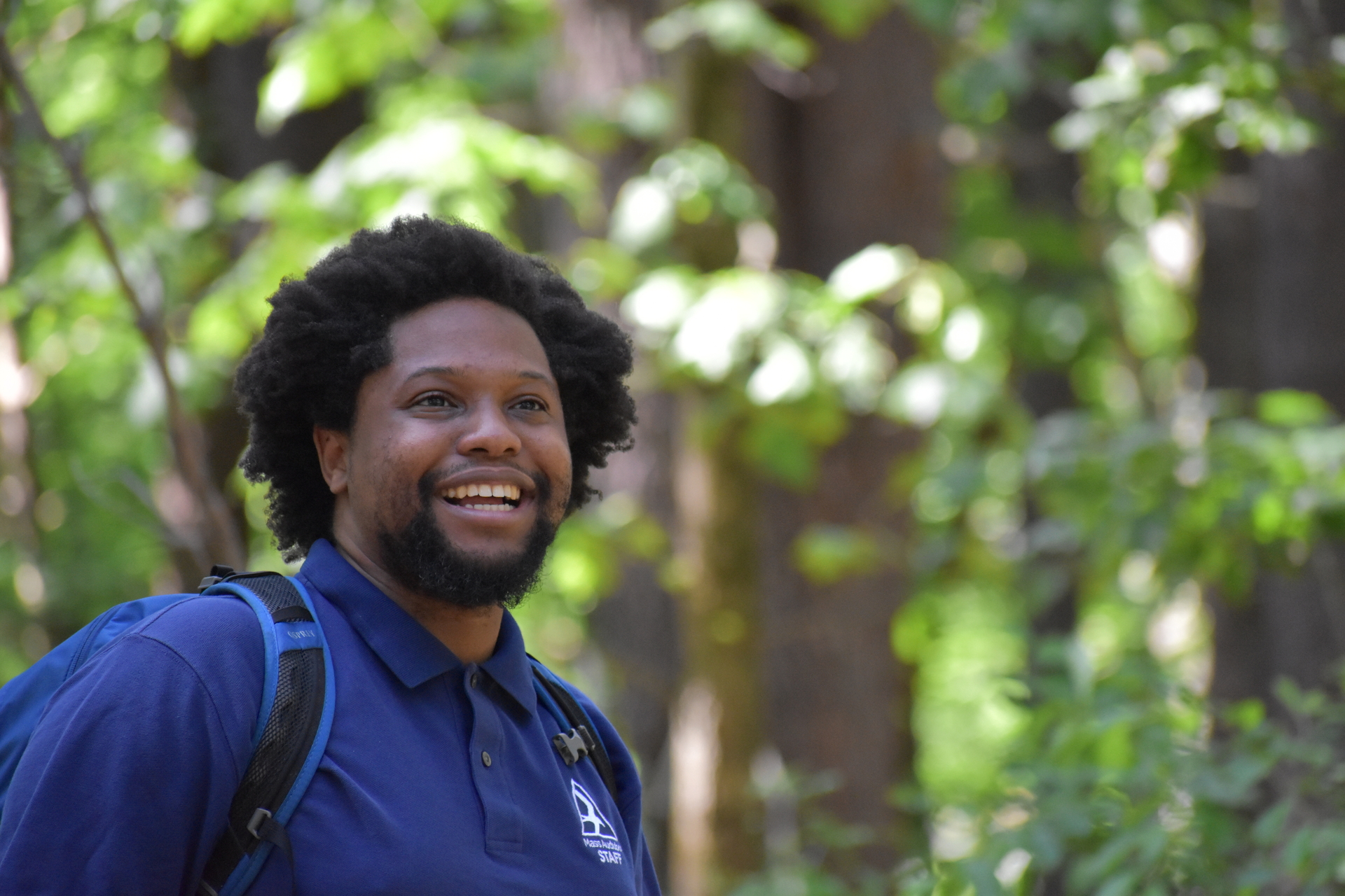 A man smiling with a blue shirt on in the woods.