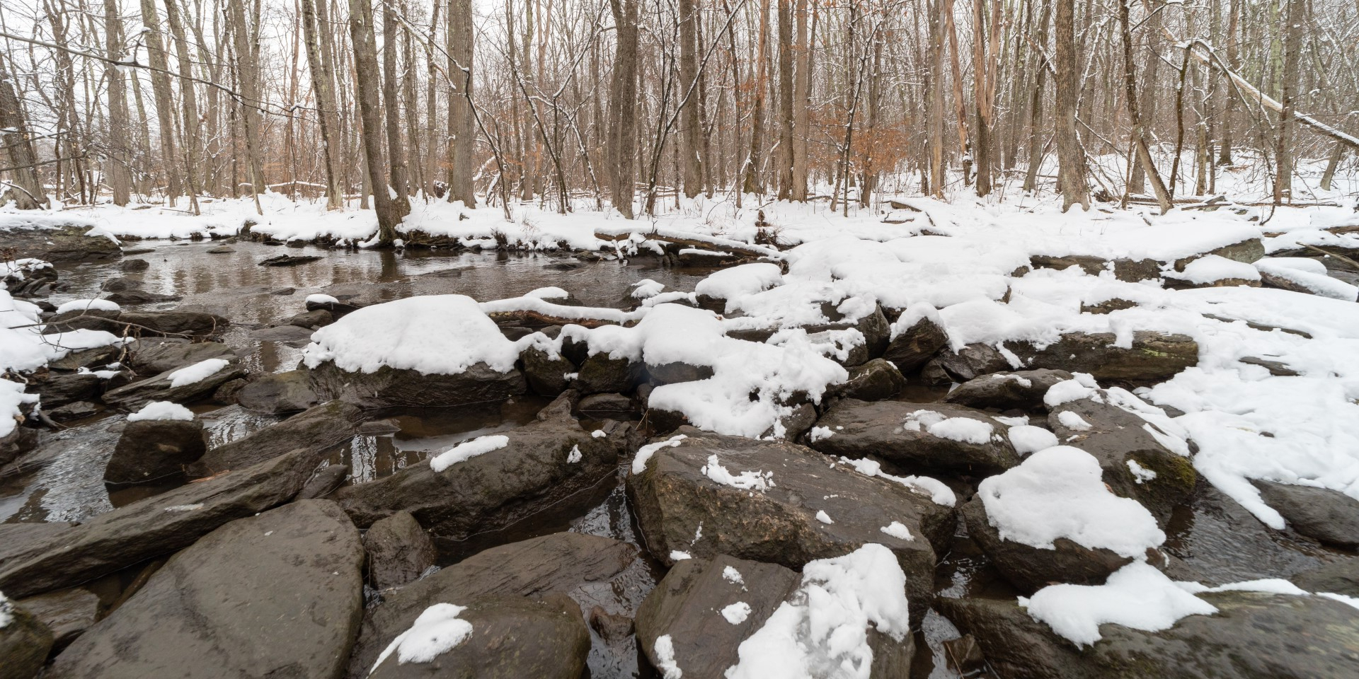 snow on rocks by river in winter