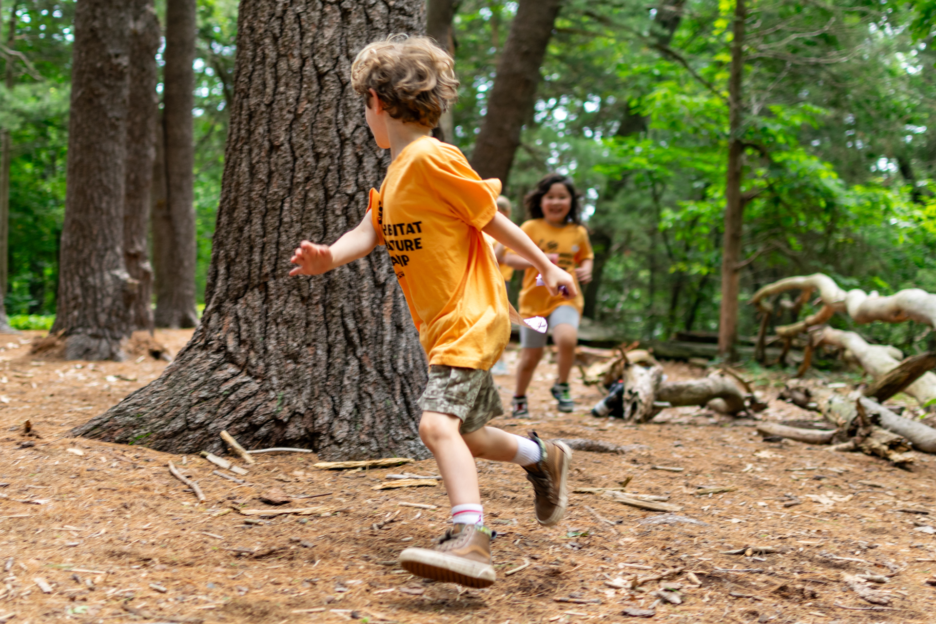 Two campers at Habitat Nature Camp running through a clearing in the woods, playing tag