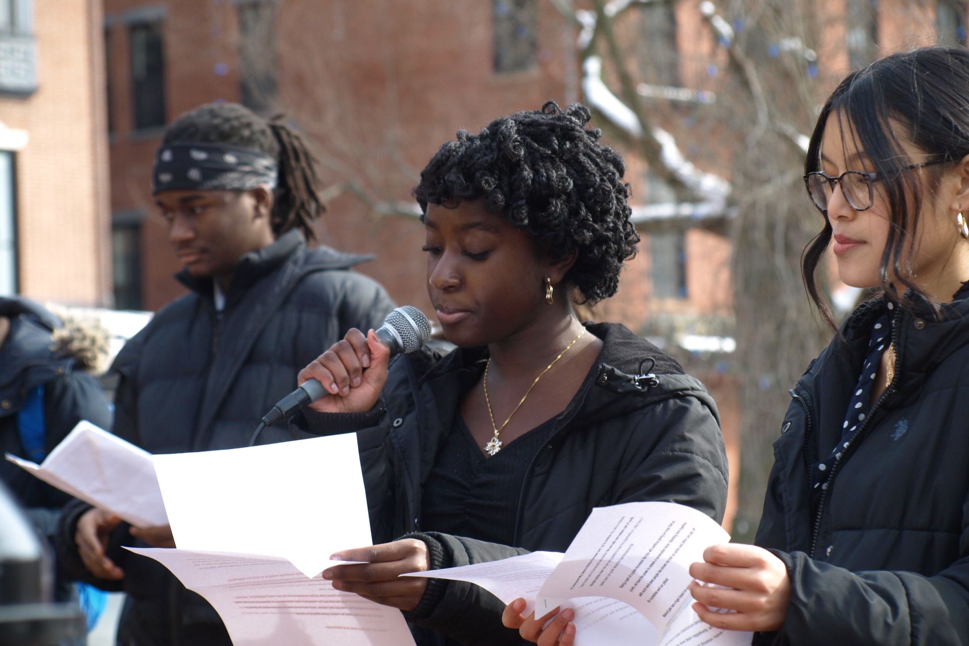 student reads from paper and speaks into microphone outside