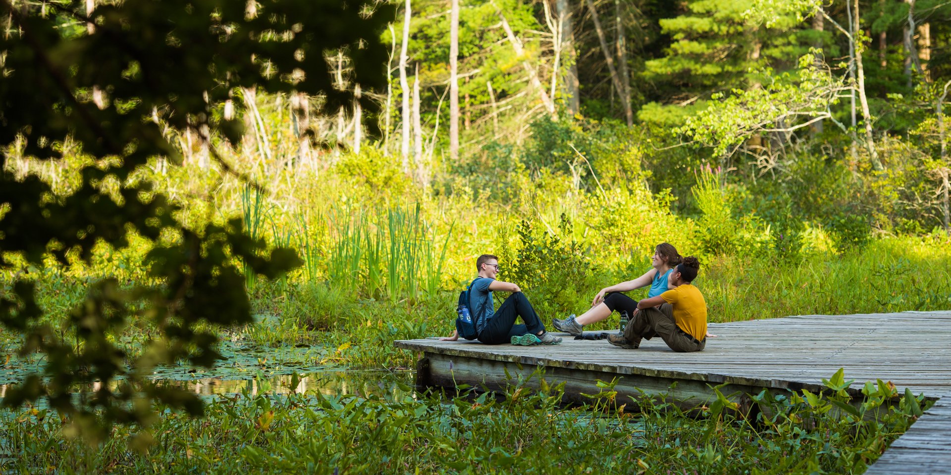 Three young adults seated on the wetlands observation platform at Broadmoor Wildlife Sanctuary in Natick