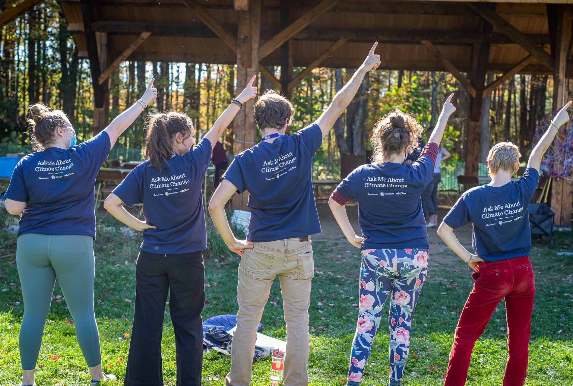 People facing away from the camera point their arms in air, wearing shirts that say "Ask Me About Climate Change"