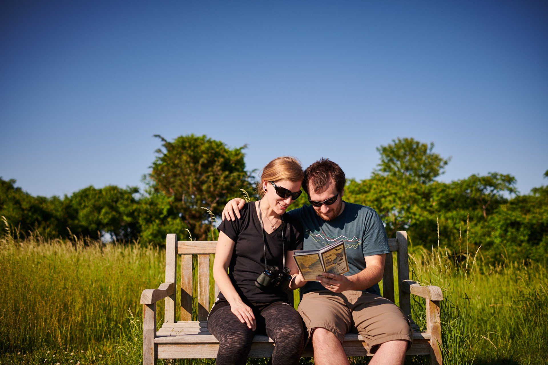 Couple sitting on bench looking at bird guide together