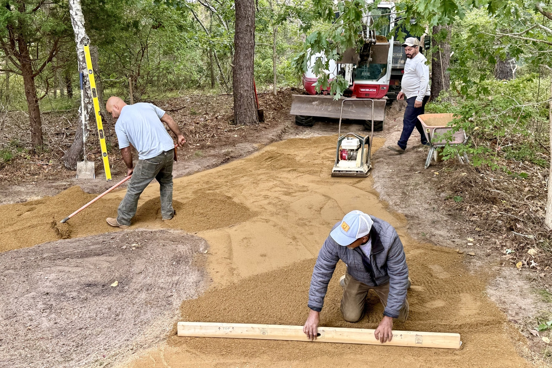 Three workers leveling sand with boards and an excavator
