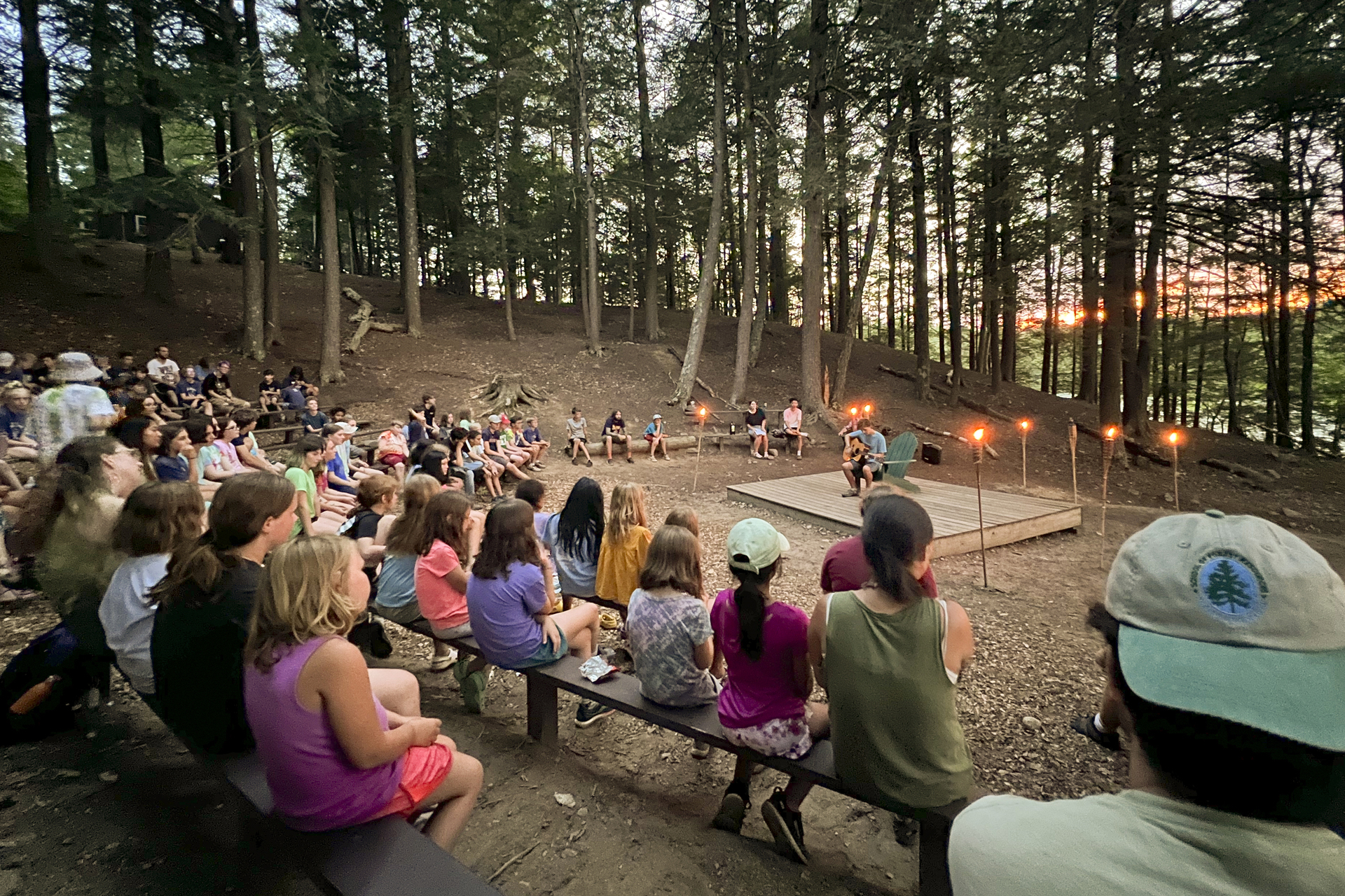 campers on benches listening to counselor playing guitar