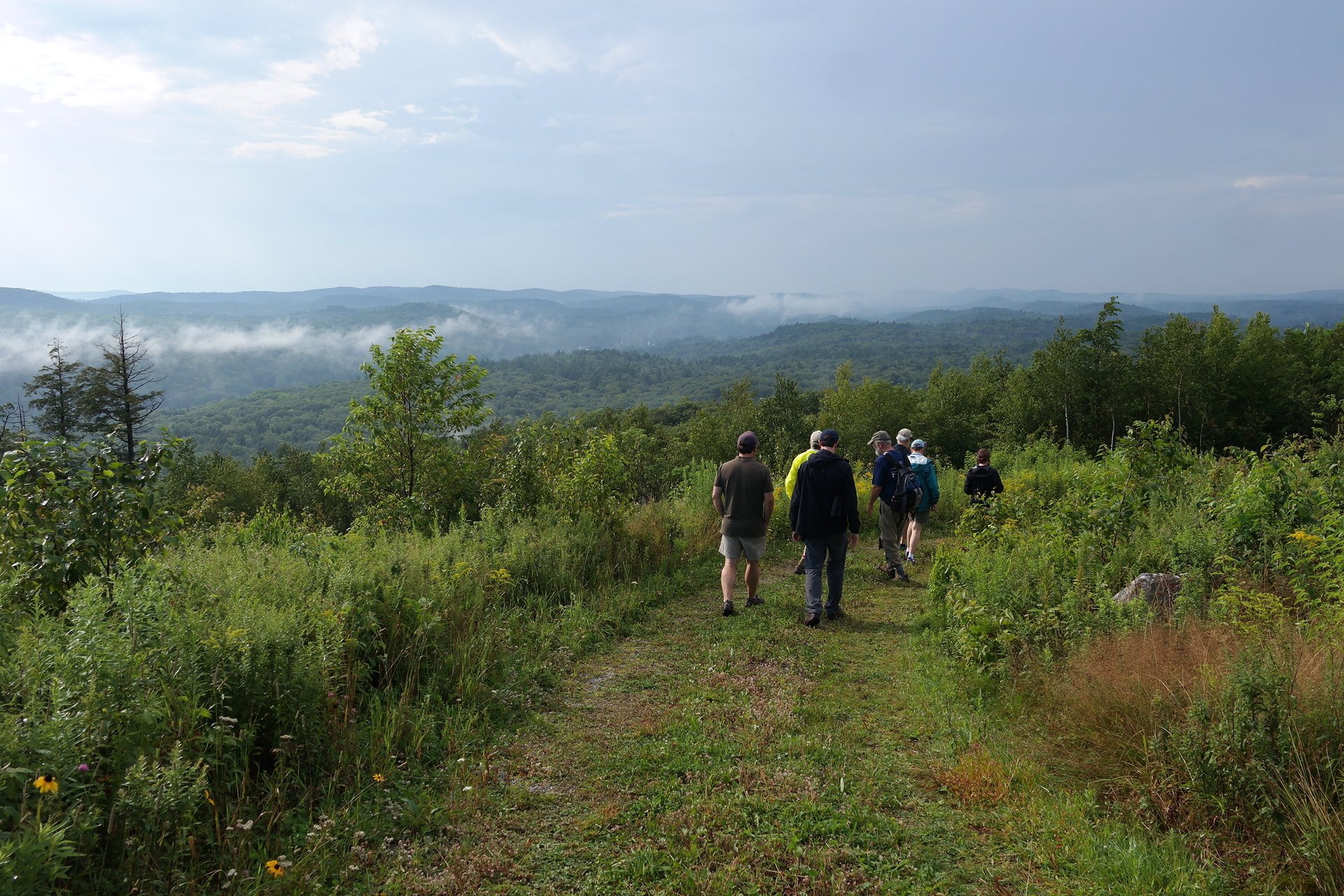 People walking on Trail  with view of clouds and mountains in the distance