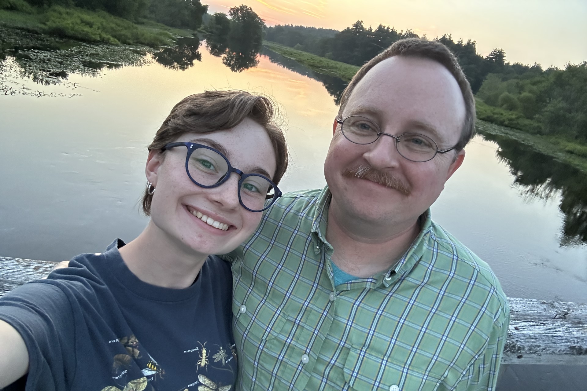 Father and daughter smiling together in front of body of water