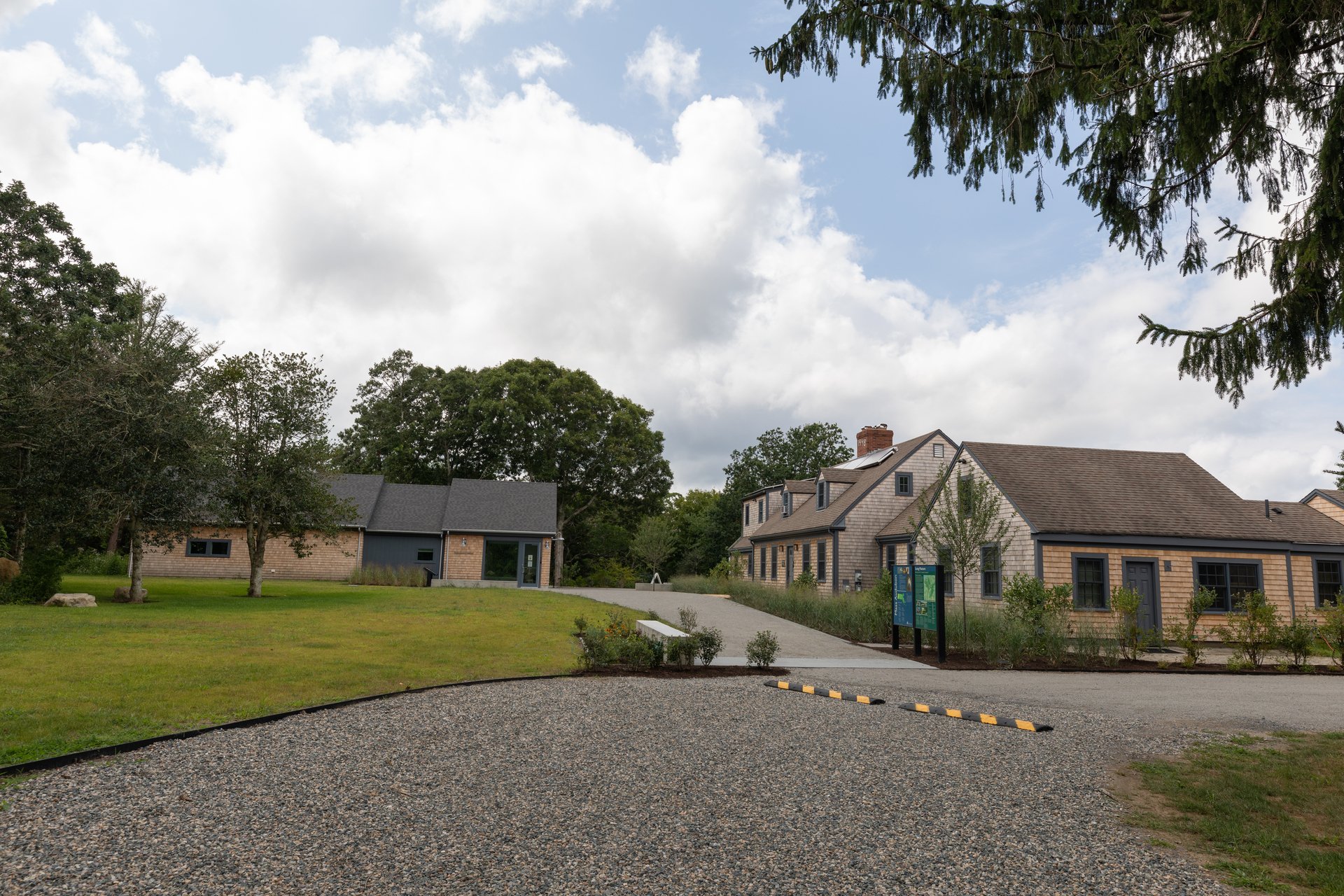 Two separate tan buildings with a walkway between them. A gravel road out front with a speed bump.