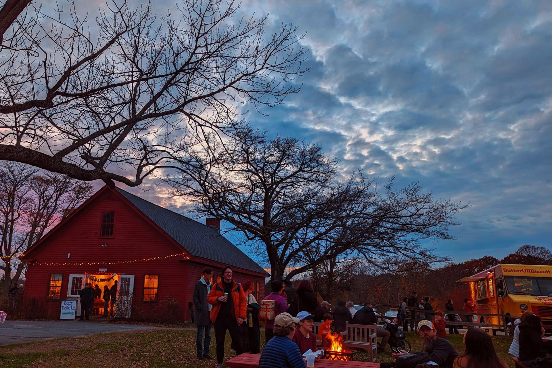 Felix Neck's Fall Fest at dusk, with people eating at picnic tables in front of food trucks