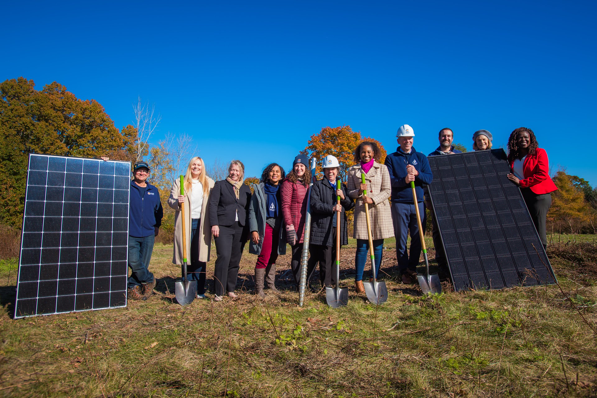 Group of people holding shovels between to solar panels
