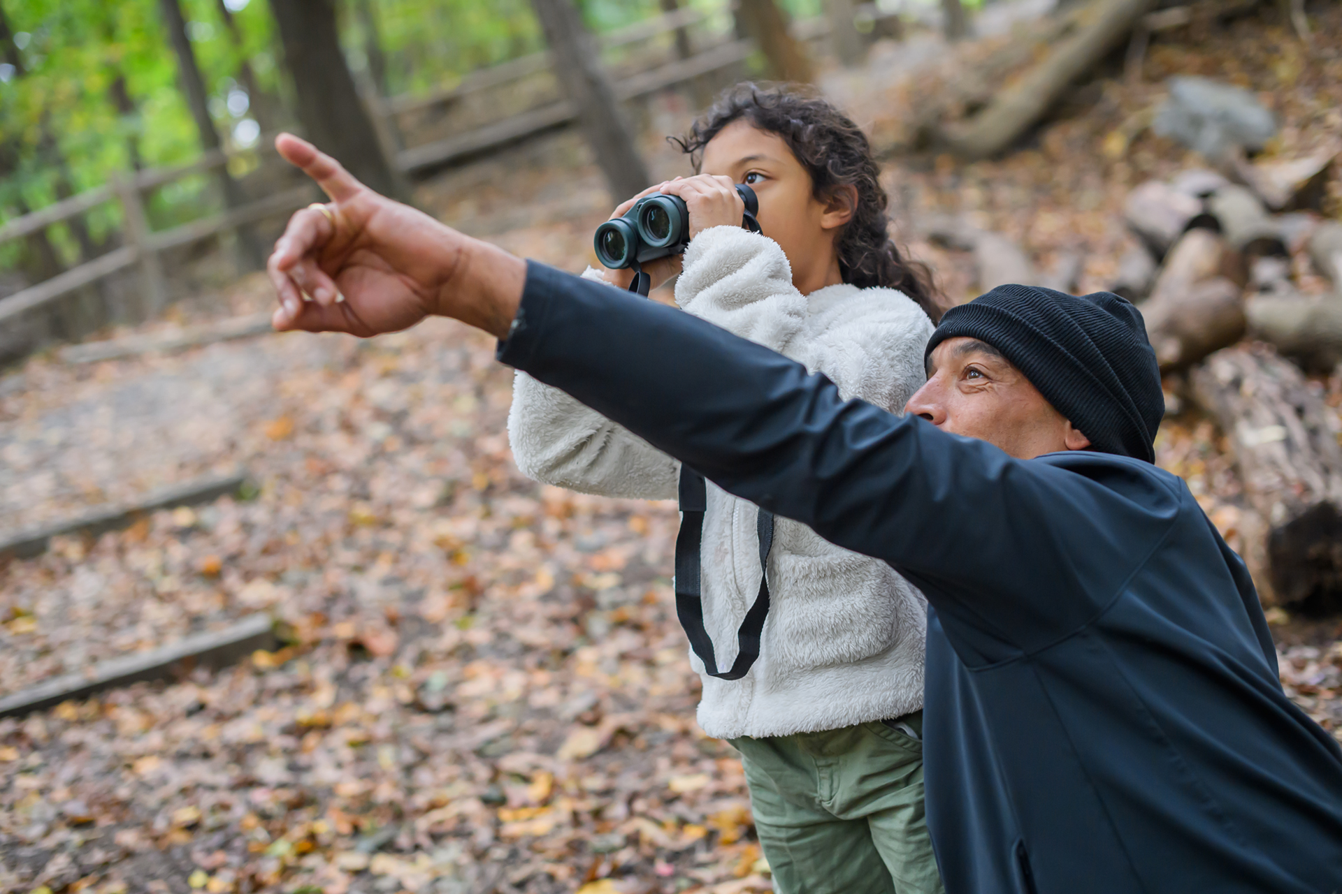 An older person pointing something out to a younger person with binoculars