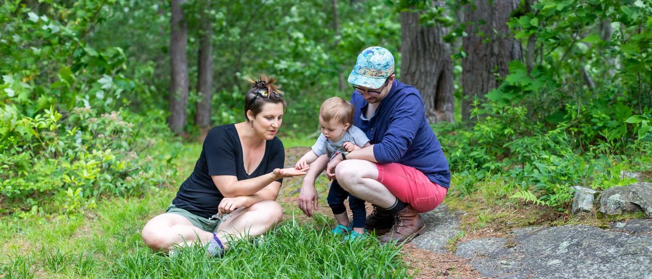 Mom, toddler, and dad looking at something found in the grass.