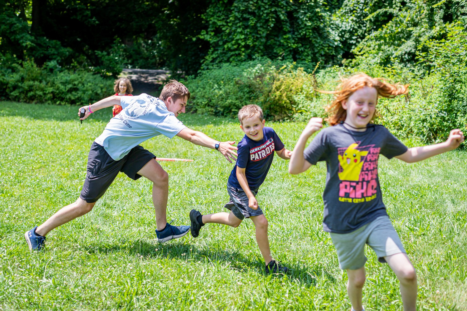 Smiling campers at Arcadia Nature Camp play tag in the grass with a counselor holding a radio