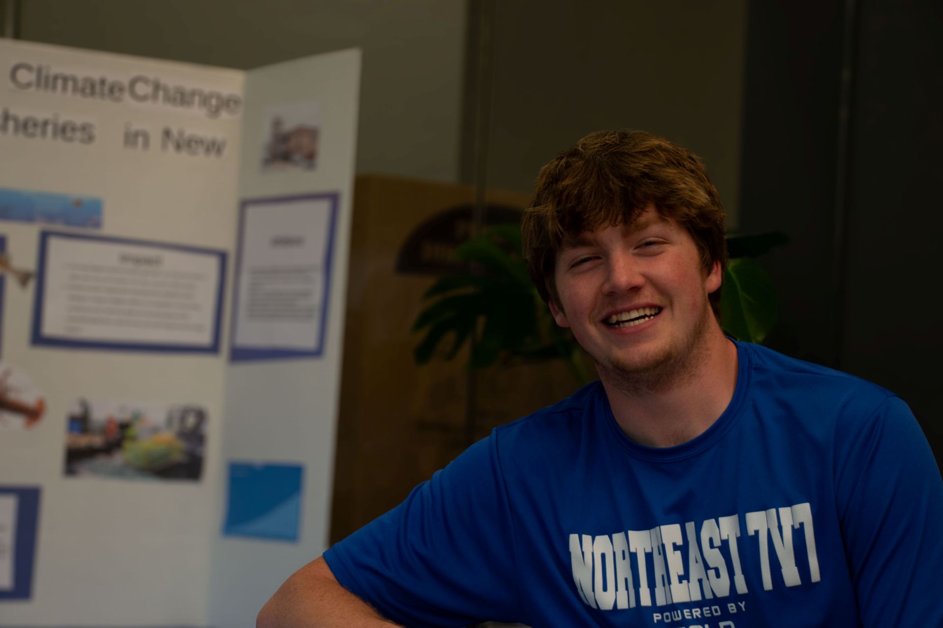 student smiles beside poster board on climate change