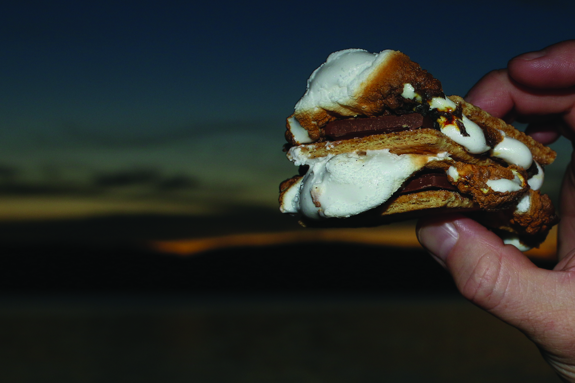 Hand holding a s'more with sunset in the background