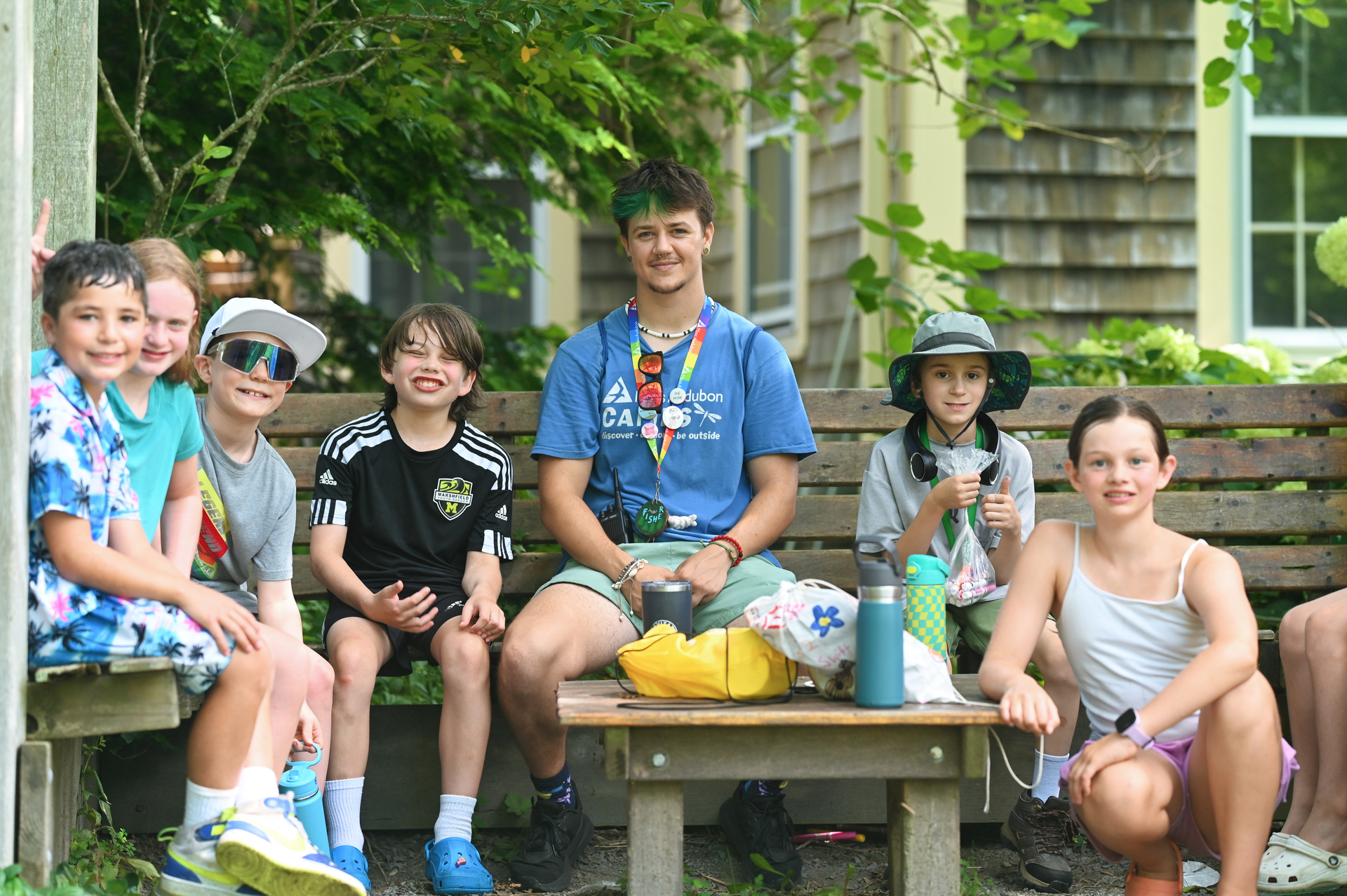 a counselor sits on a bench with a group of campers smiling and eating snacks