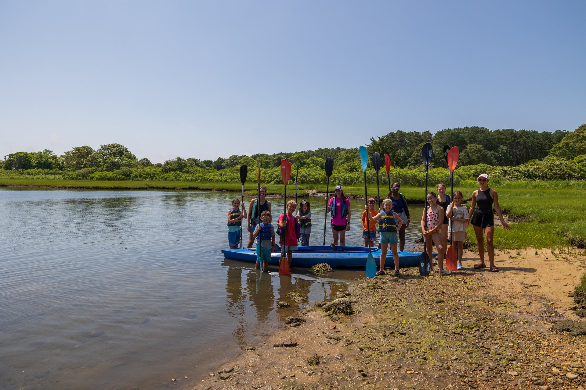 A group of counselors and campers stand beside a kayak smiling at camera.