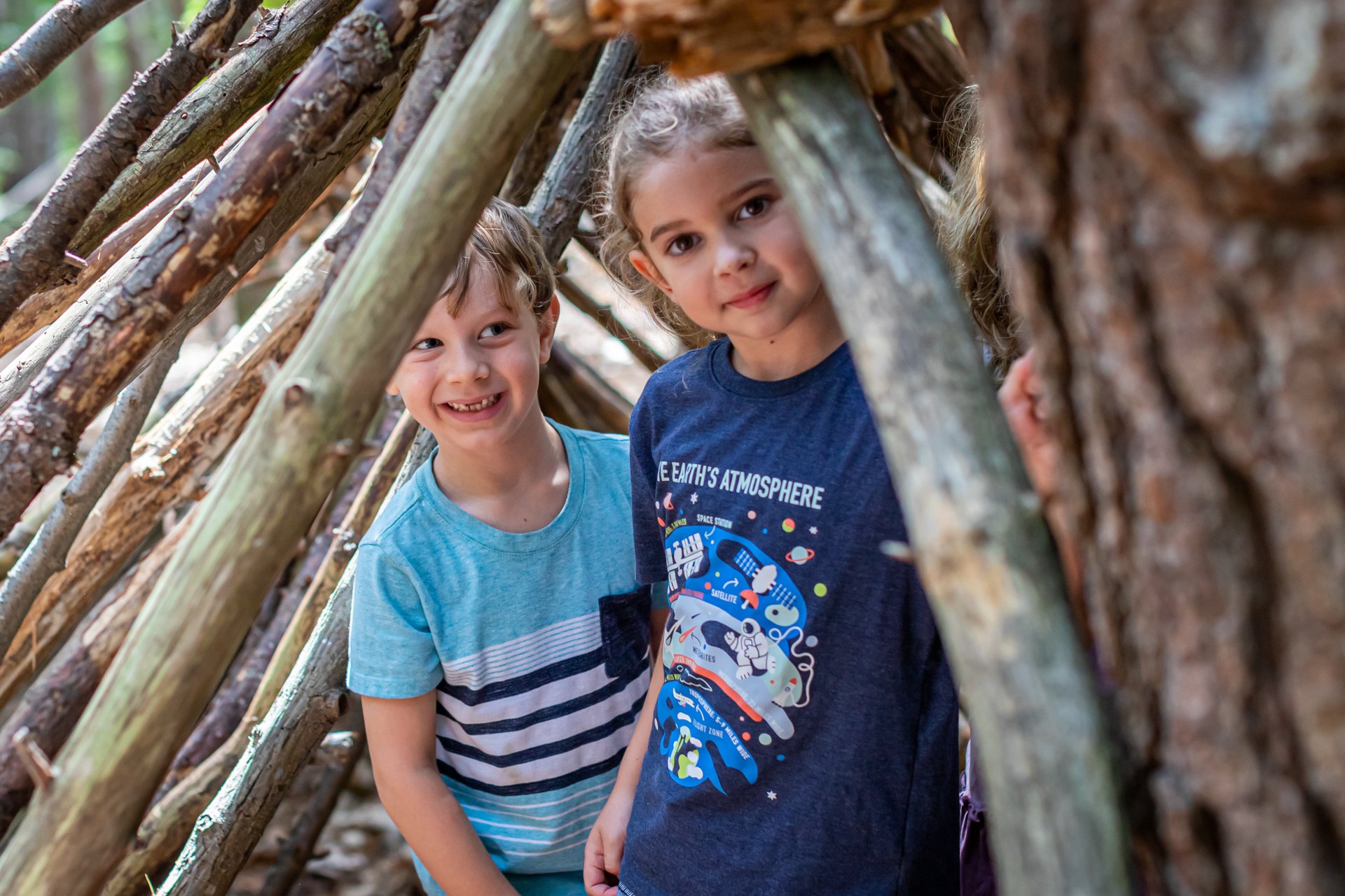 Two campers at Arcadia Nature Camp play inside a shelter built of branches