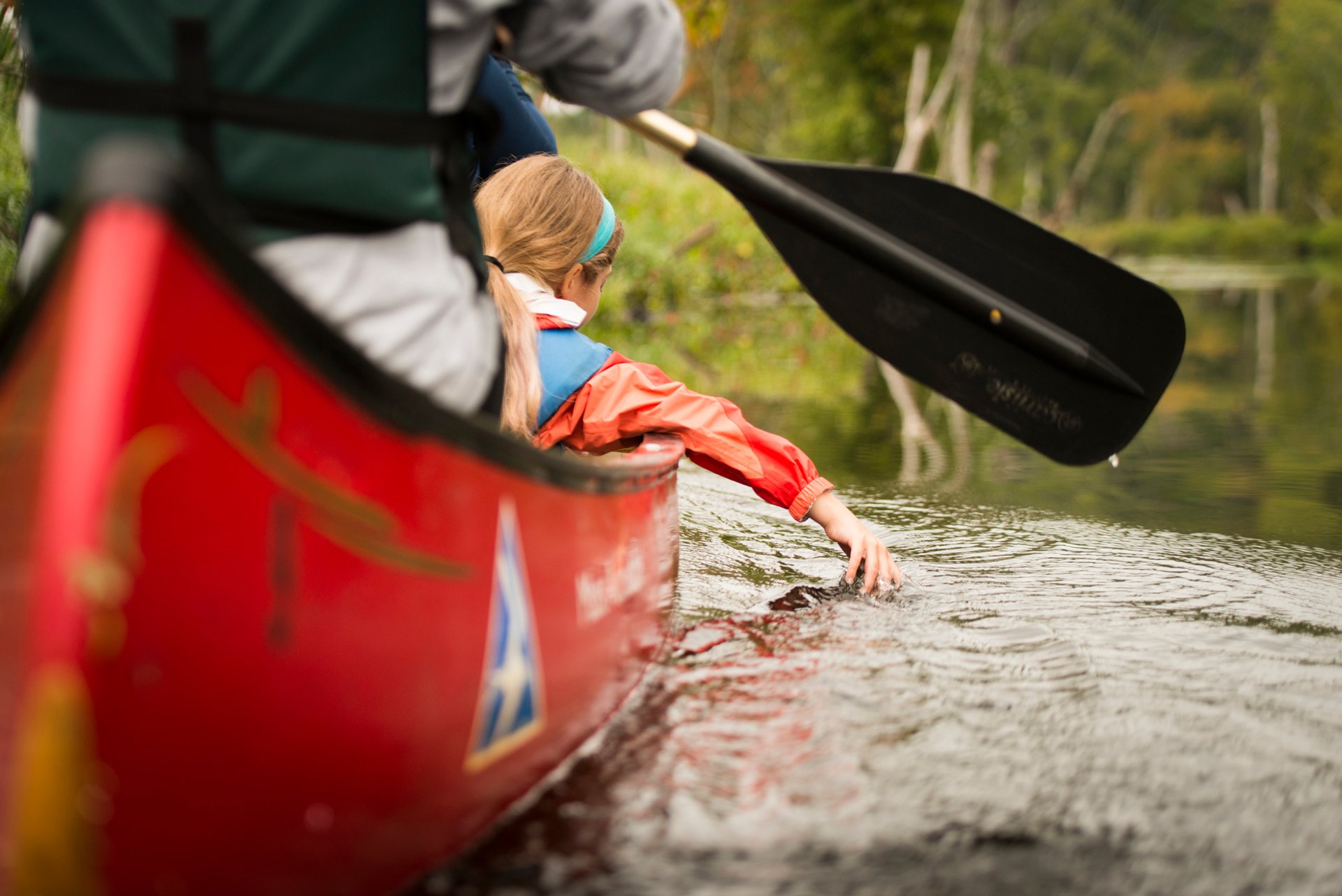 view from the water of man and child in canoe, child's hand touching the water