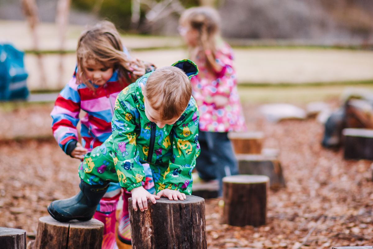 Stony Brook Preschoolers in nature play area climbing on stumps