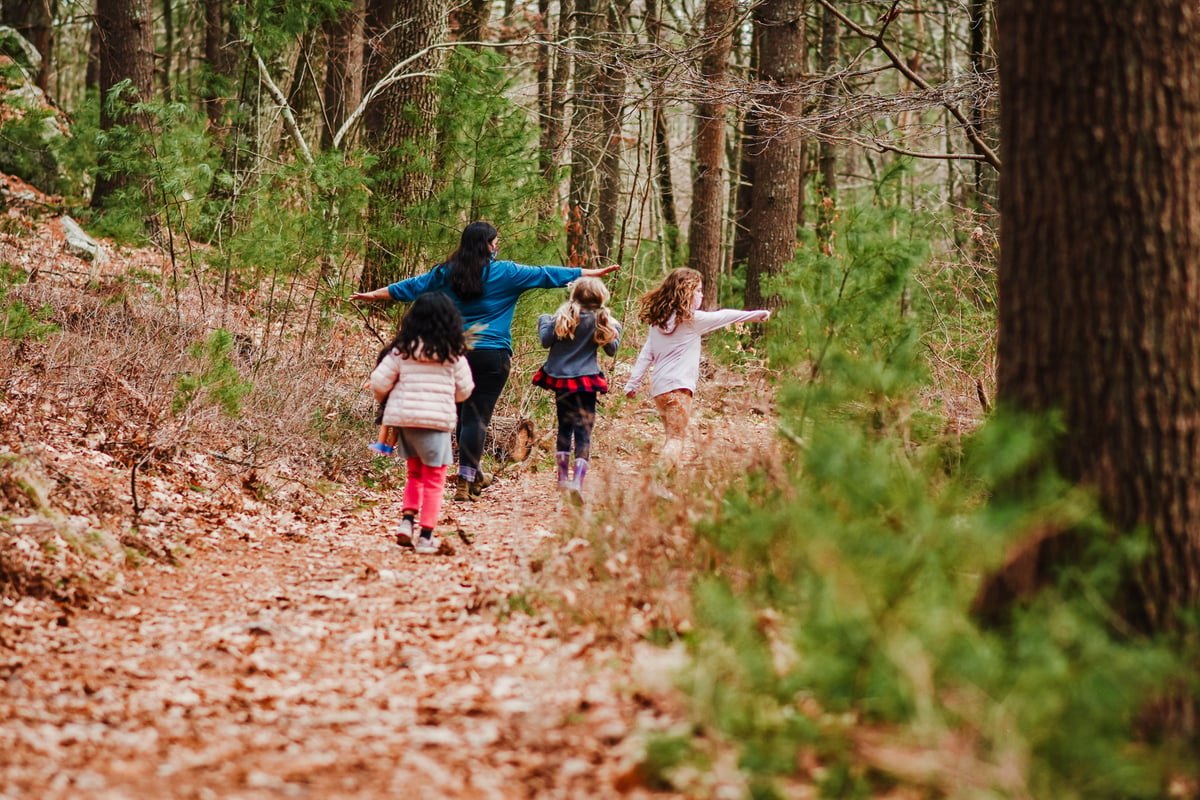 Three kids with an adult in a blue sweatshirt on a trail covered with leaves.
