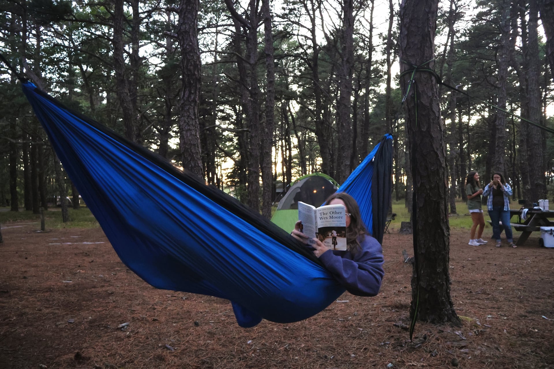 Person lounging in a blue hammock while reading a book