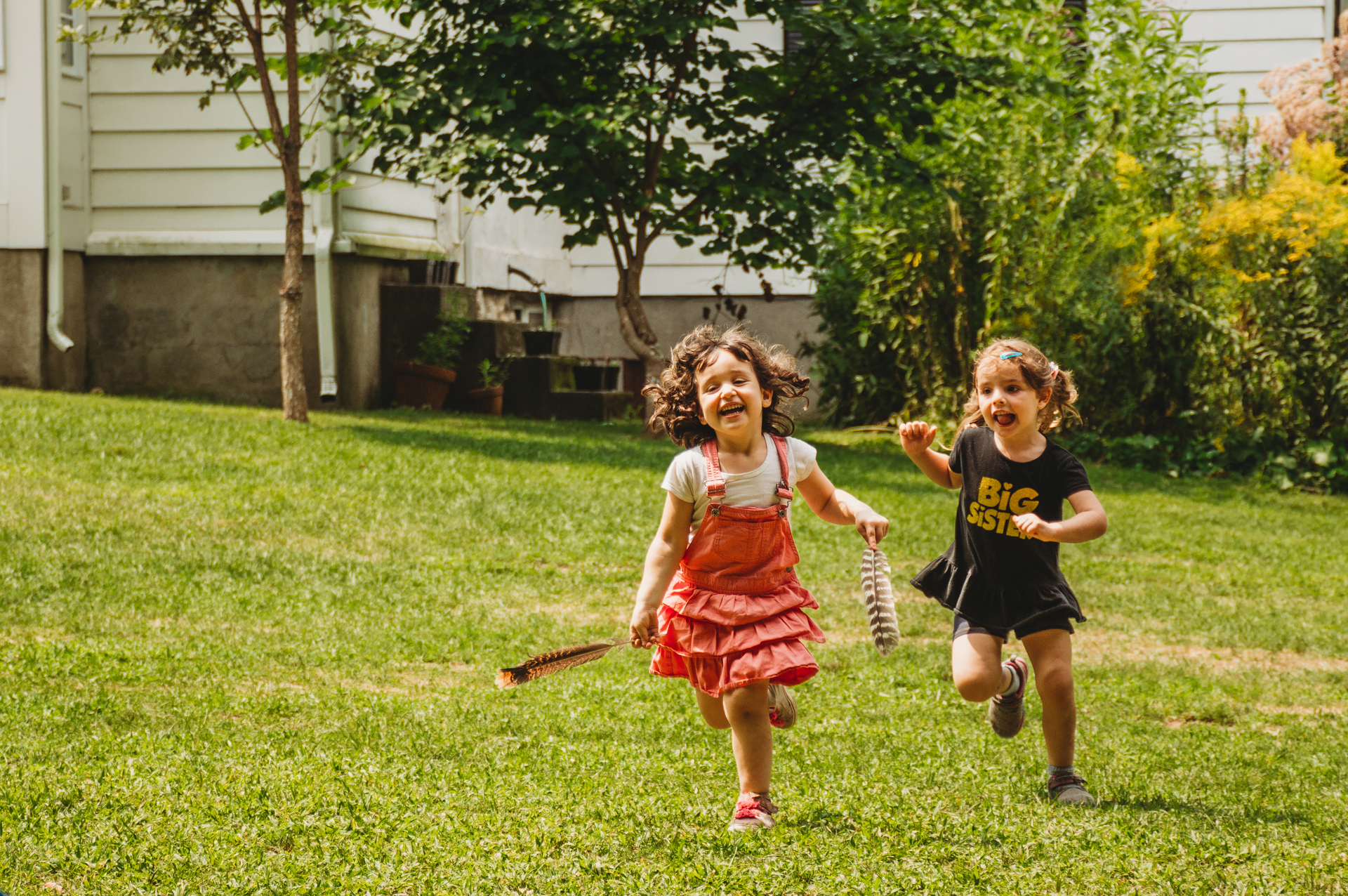 Two smiling campers at Moose Hill Nature Camp running across a lawn carrying bird feathers