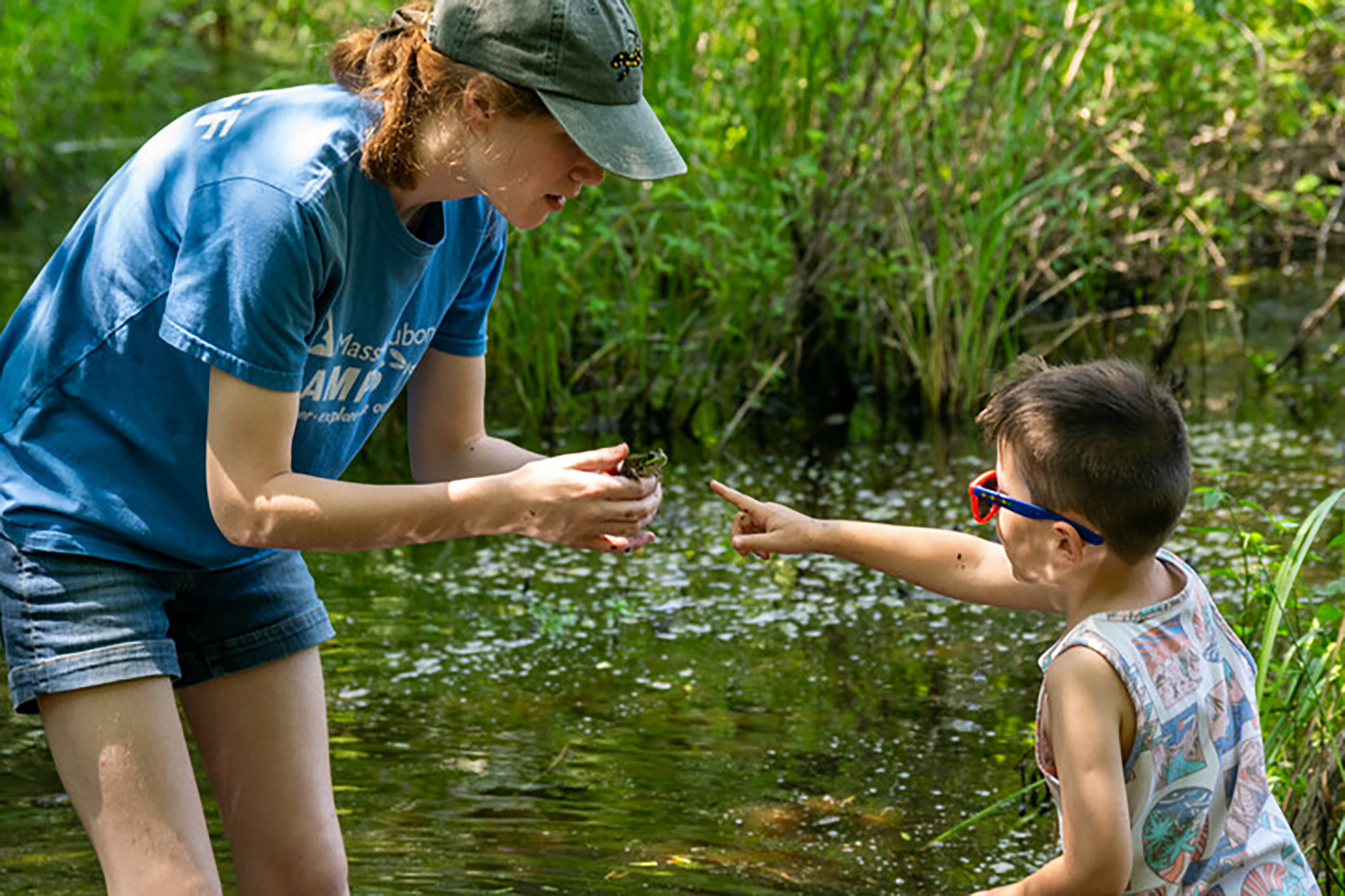Camper and counselor inspecting something by the pond