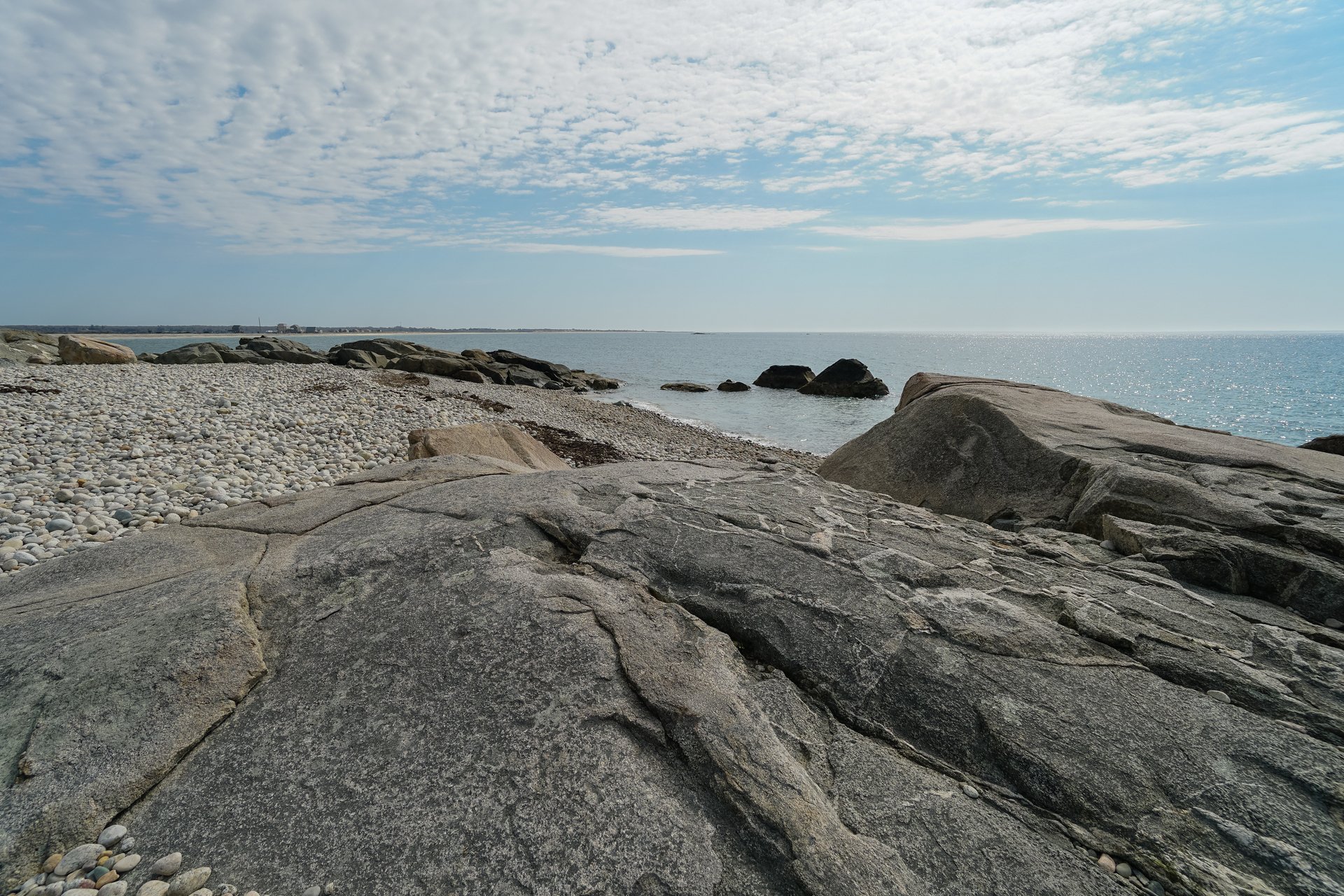 A rocky ledge overlooking the pebble-covered shoreline. Large, sharp rocks stick out of the water.
