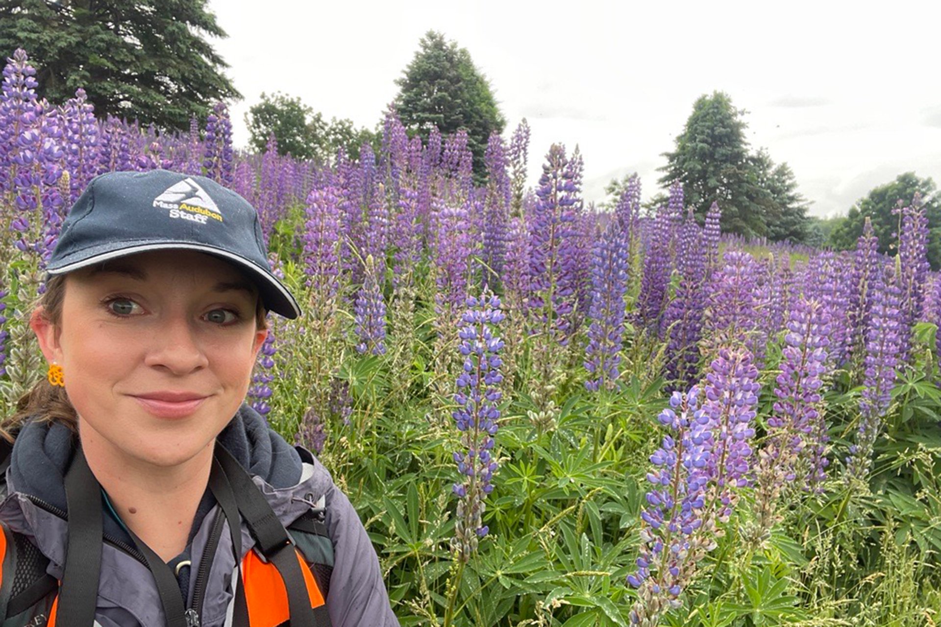 Nicole Marcotte wearing a blue cap, taking a selfie in front of a field of purple flowers