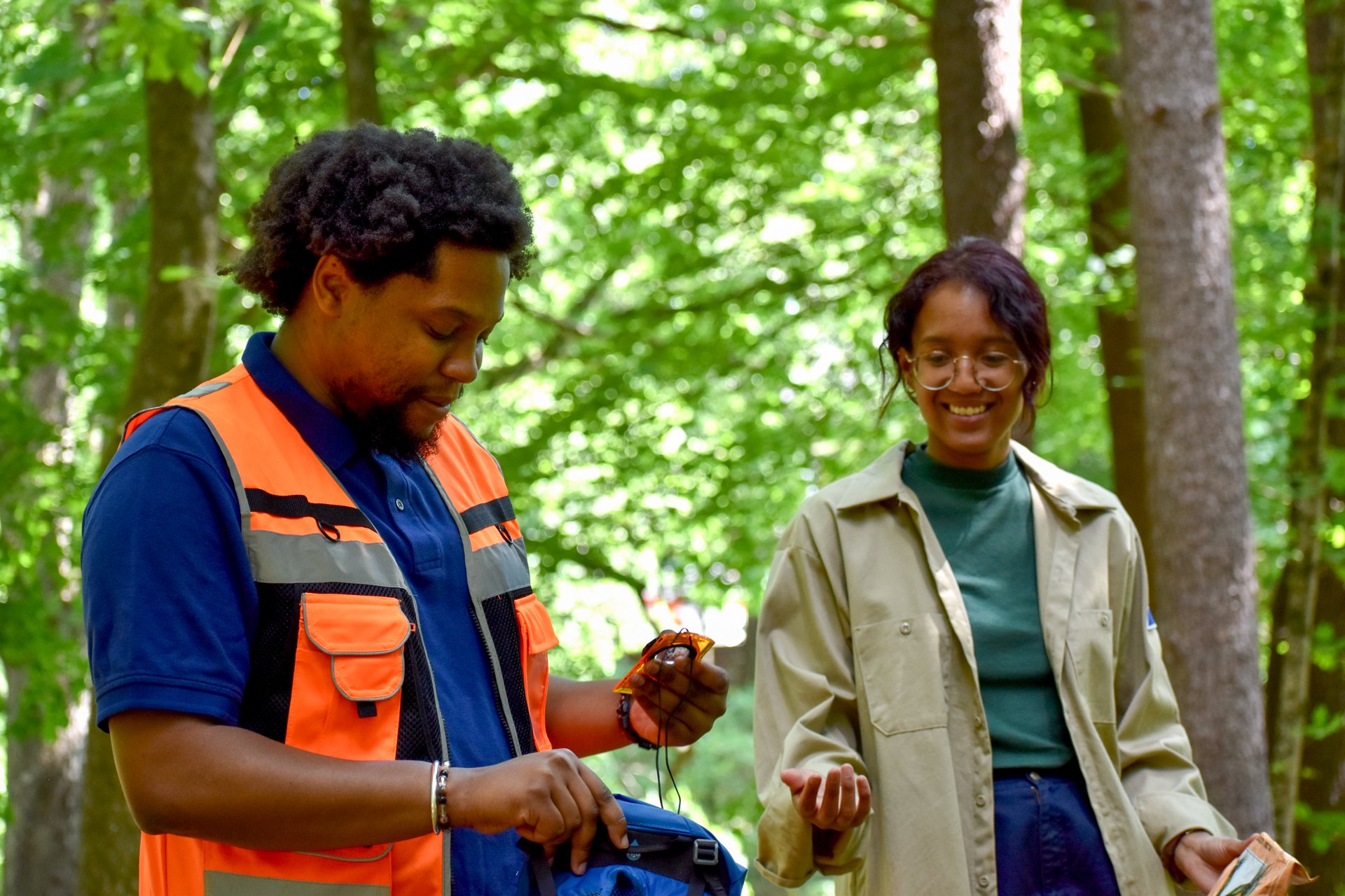 Two Fellows from the Environmental Fellowship Program in a lush, green forest, wearing field dress and holding a compass for navigation