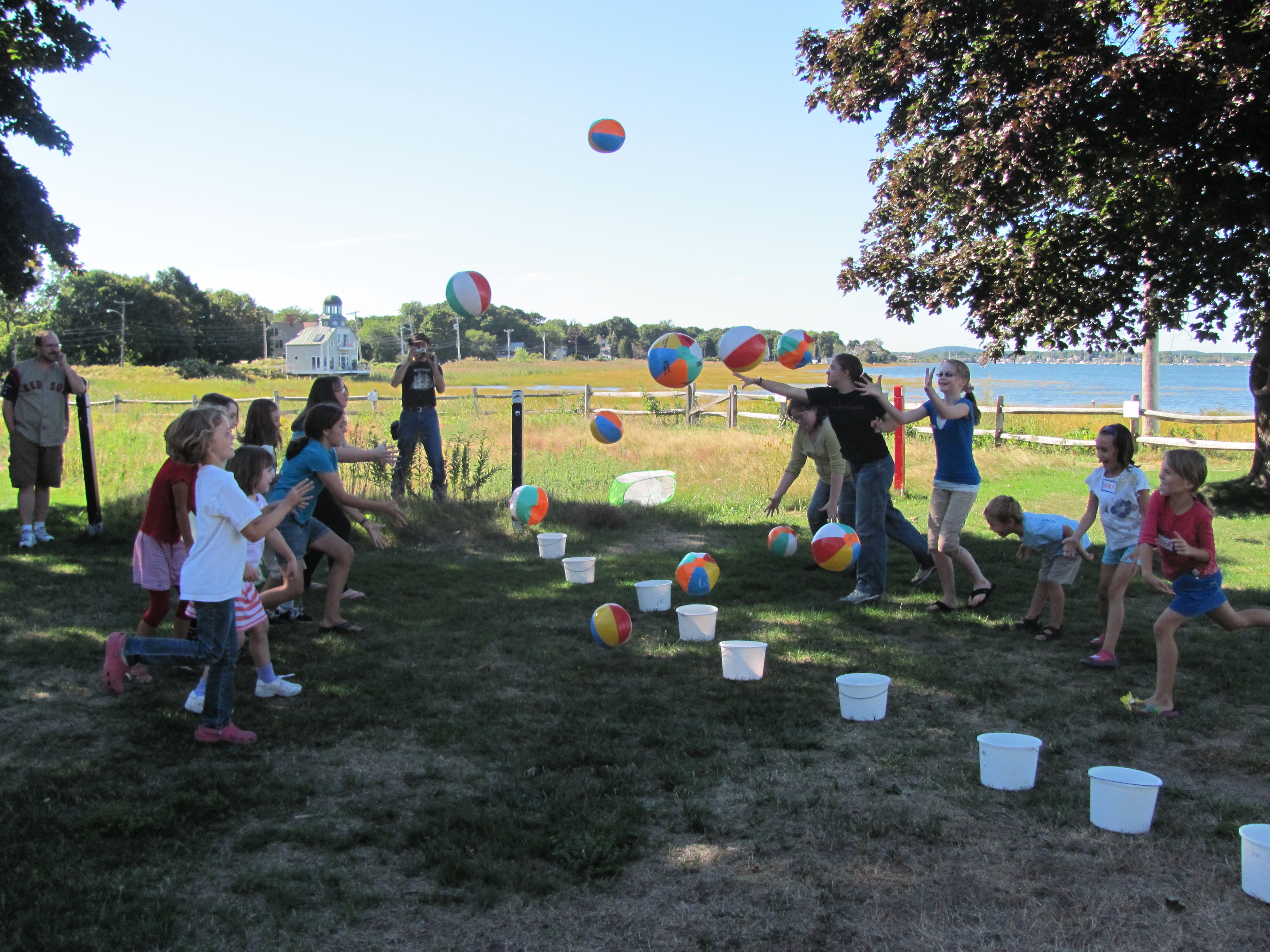 Children tossing beach balls to one another across a line of white buckets