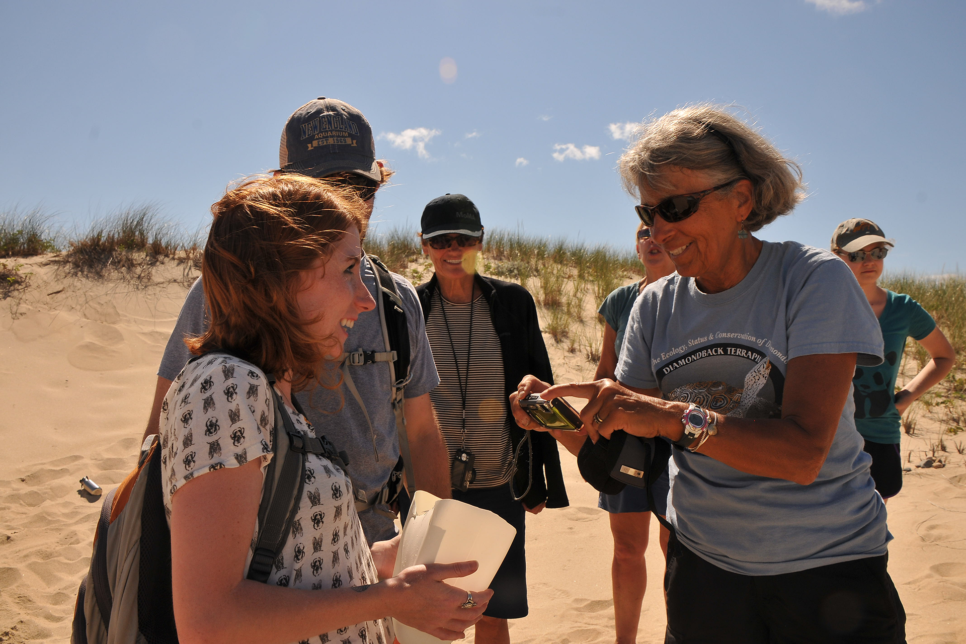 Woman with a blue shirt and sunglasses takes a picture of something in a plastic container. A woman smiles while holding the container.