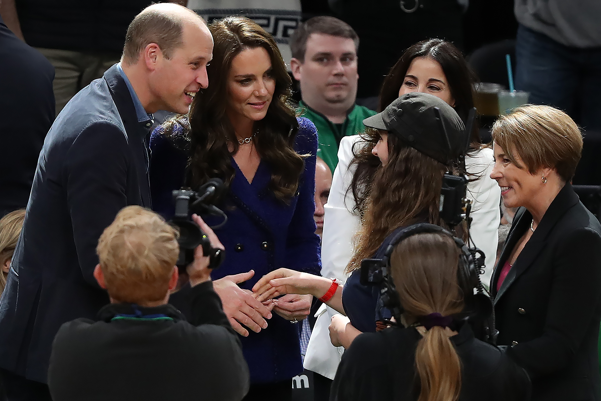 Prince William extends his hand to shake Ollie Perrault's hand. Princess Kate stands next to her husband smiling at Ollie. Cameramen surround them to take a photo of the interaction.