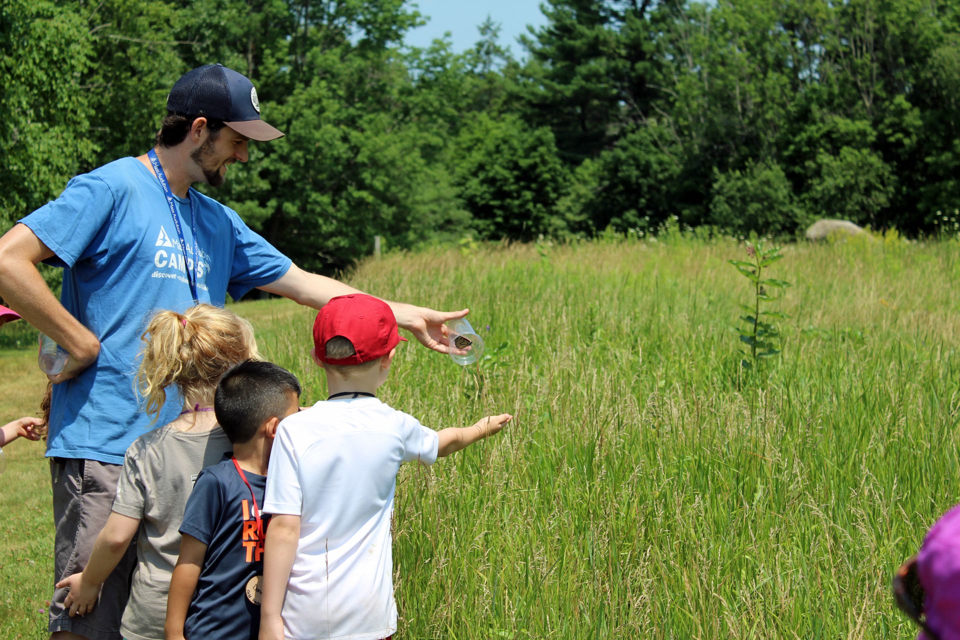 A counselor releases a bug into a field with three small campers.